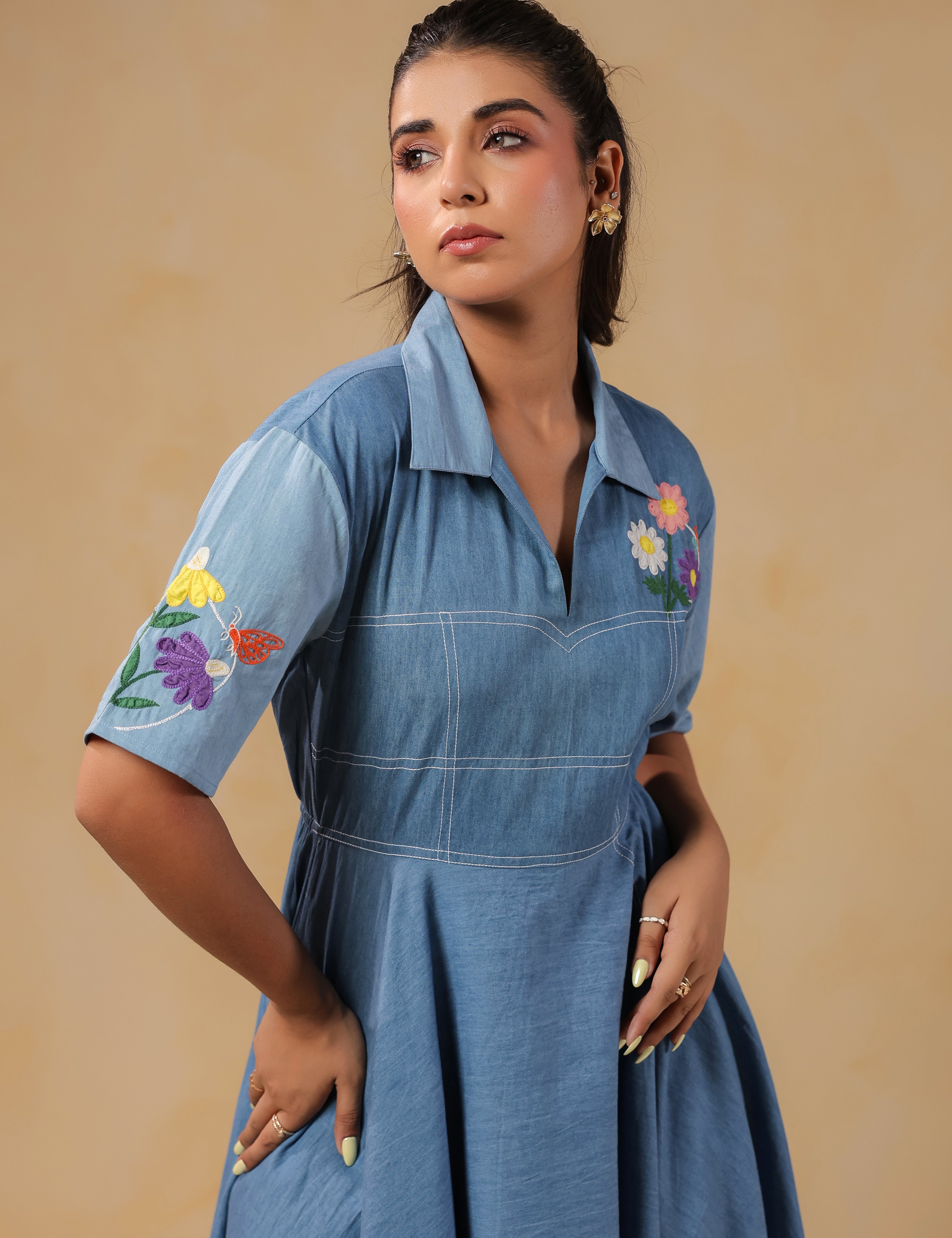 Close-up of the Daisydrift Handkerchief Dress sleeve with intricate multicolor floral embroidery and a delicate butterfly motif on soft blue denim fabric.