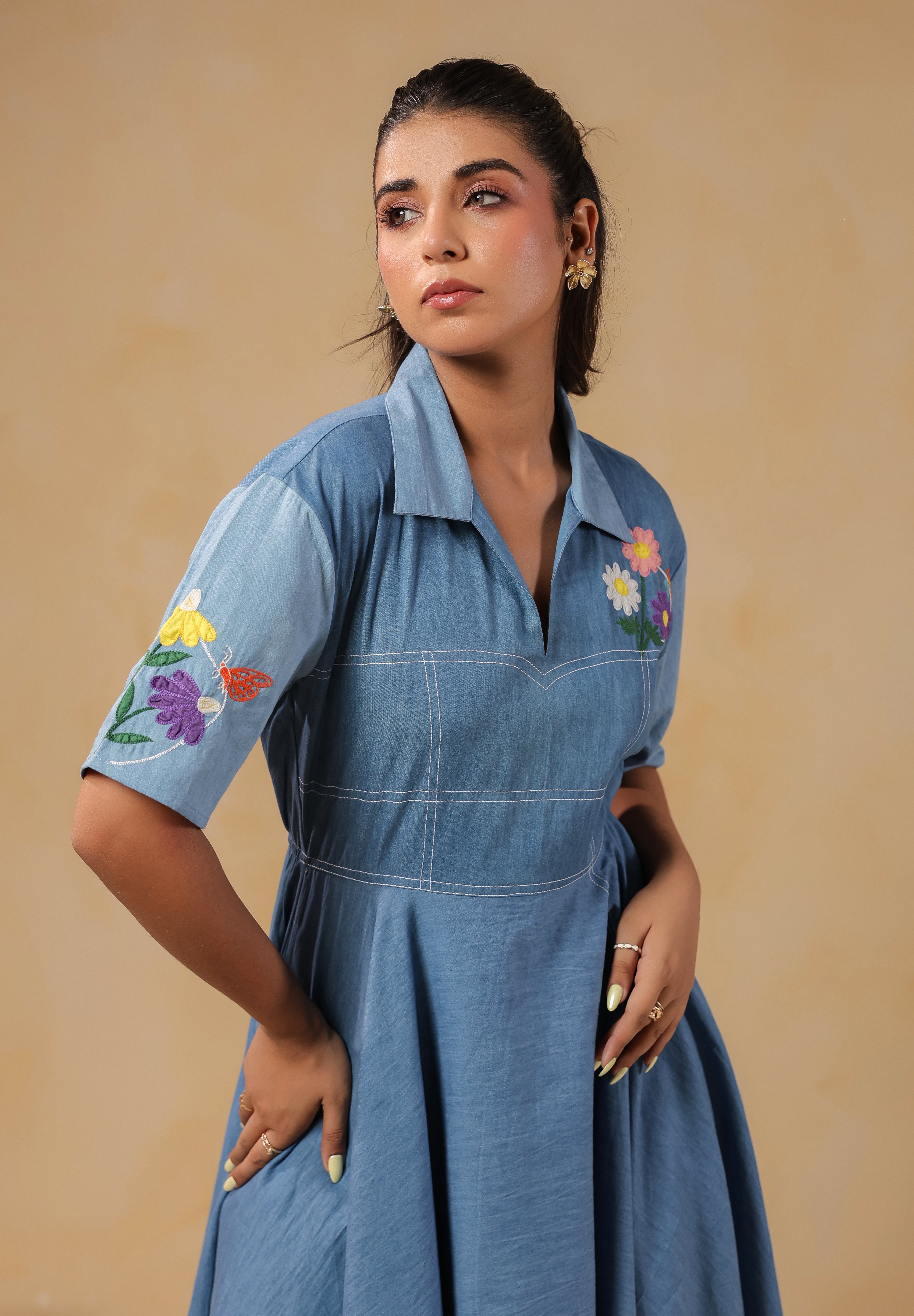 Close-up of the Daisydrift Handkerchief Dress sleeve with intricate multicolor floral embroidery and a delicate butterfly motif on soft blue denim fabric.