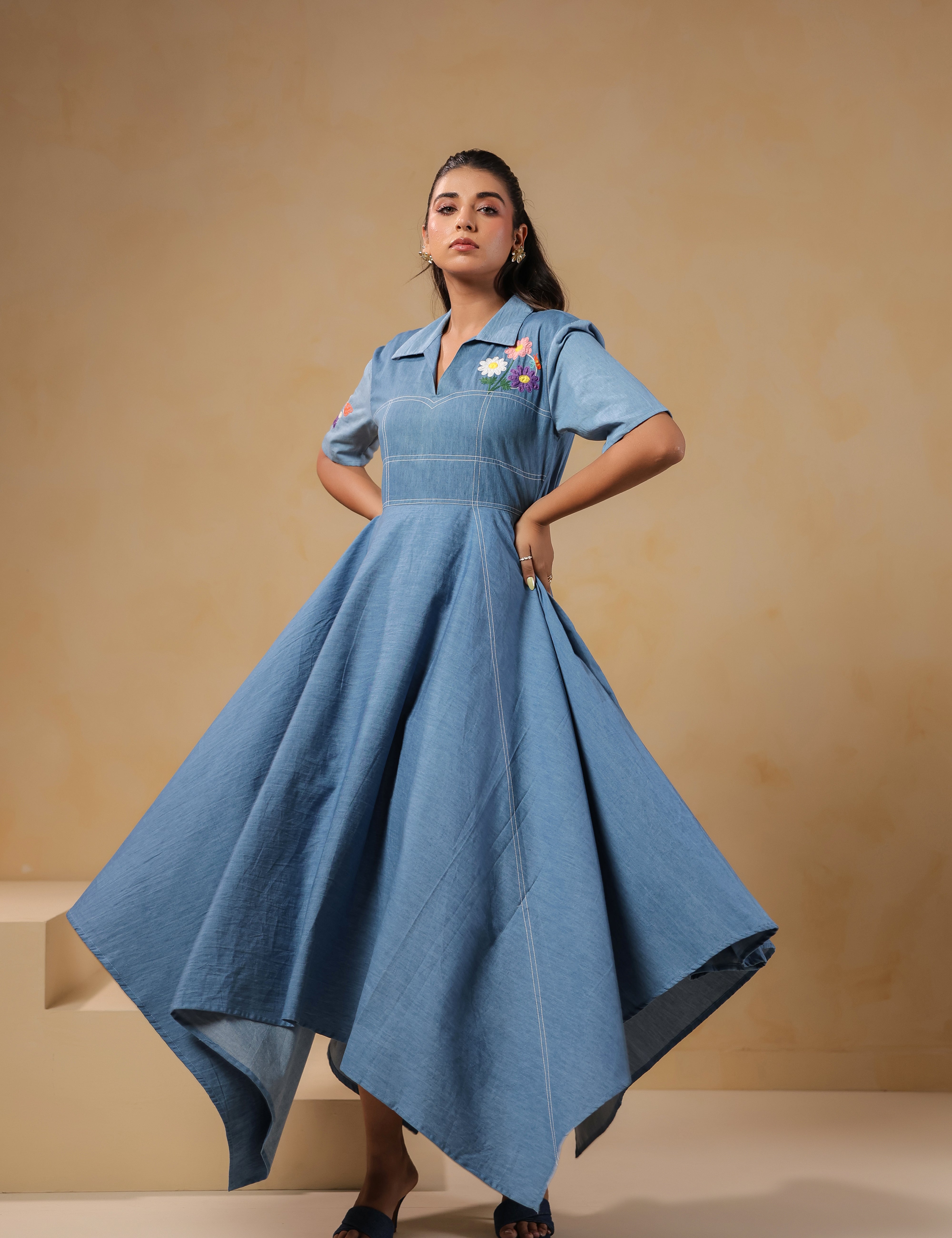 Model wearing the Daisydrift Handkerchief Dress in soft denim, showcasing a dramatic handkerchief hem and structured fit with floral embroidery on the chest.