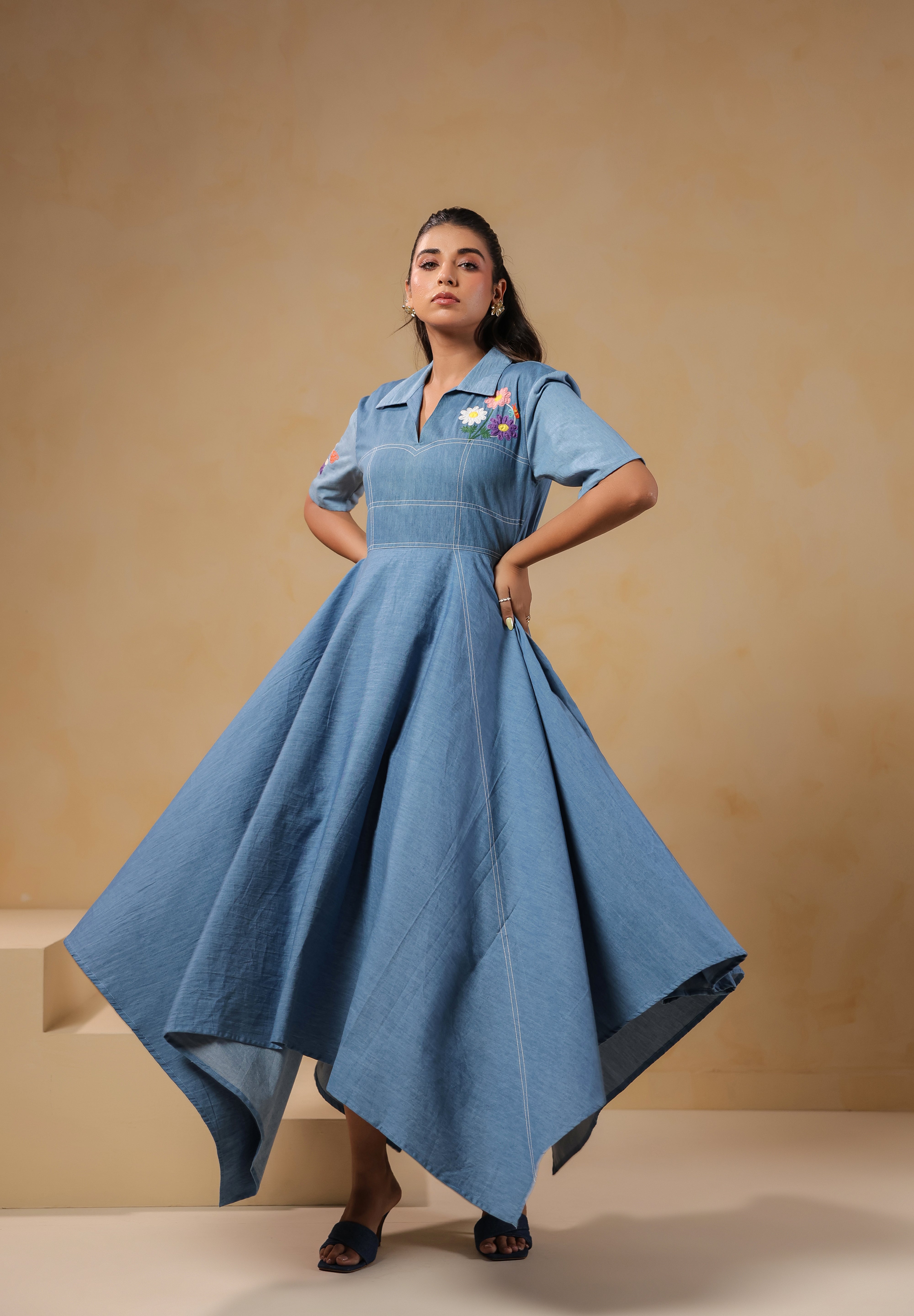 Model wearing the Daisydrift Handkerchief Dress in soft denim, showcasing a dramatic handkerchief hem and structured fit with floral embroidery on the chest.
