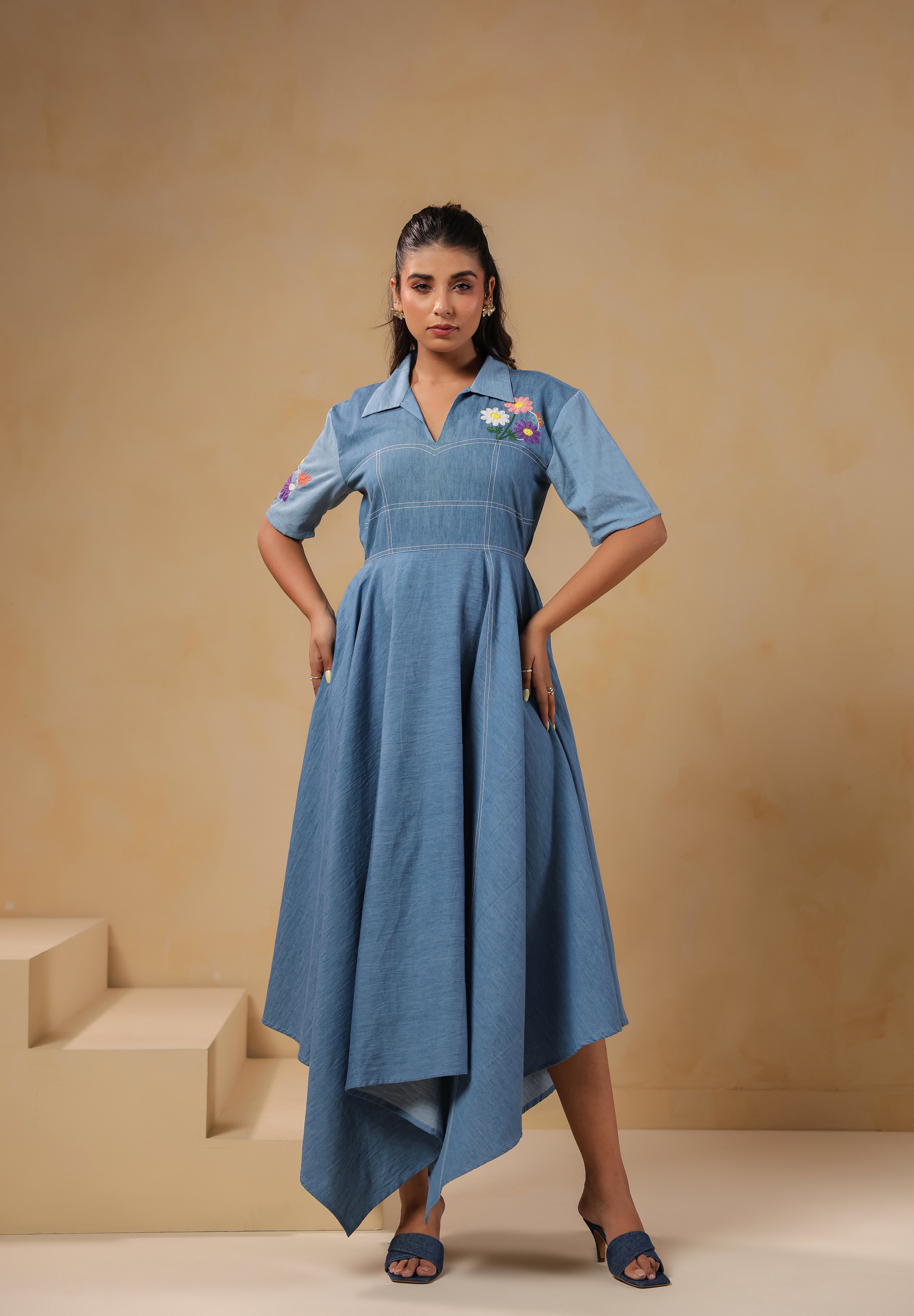 Model posing in the Daisydrift Handkerchief Dress, showing the structured bodice, short sleeves, floral detailing, and flared handkerchief hemline in soft denim.