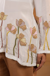 Close-up of a white garment with floral embroidery on a neutral background