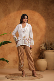 Woman in a white blouse and beige pants standing against an orange wall with plants.