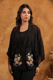 Woman wearing a black outfit with floral embroidery against a brown background