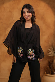Woman wearing a black outfit with floral embroidery against a warm brown background