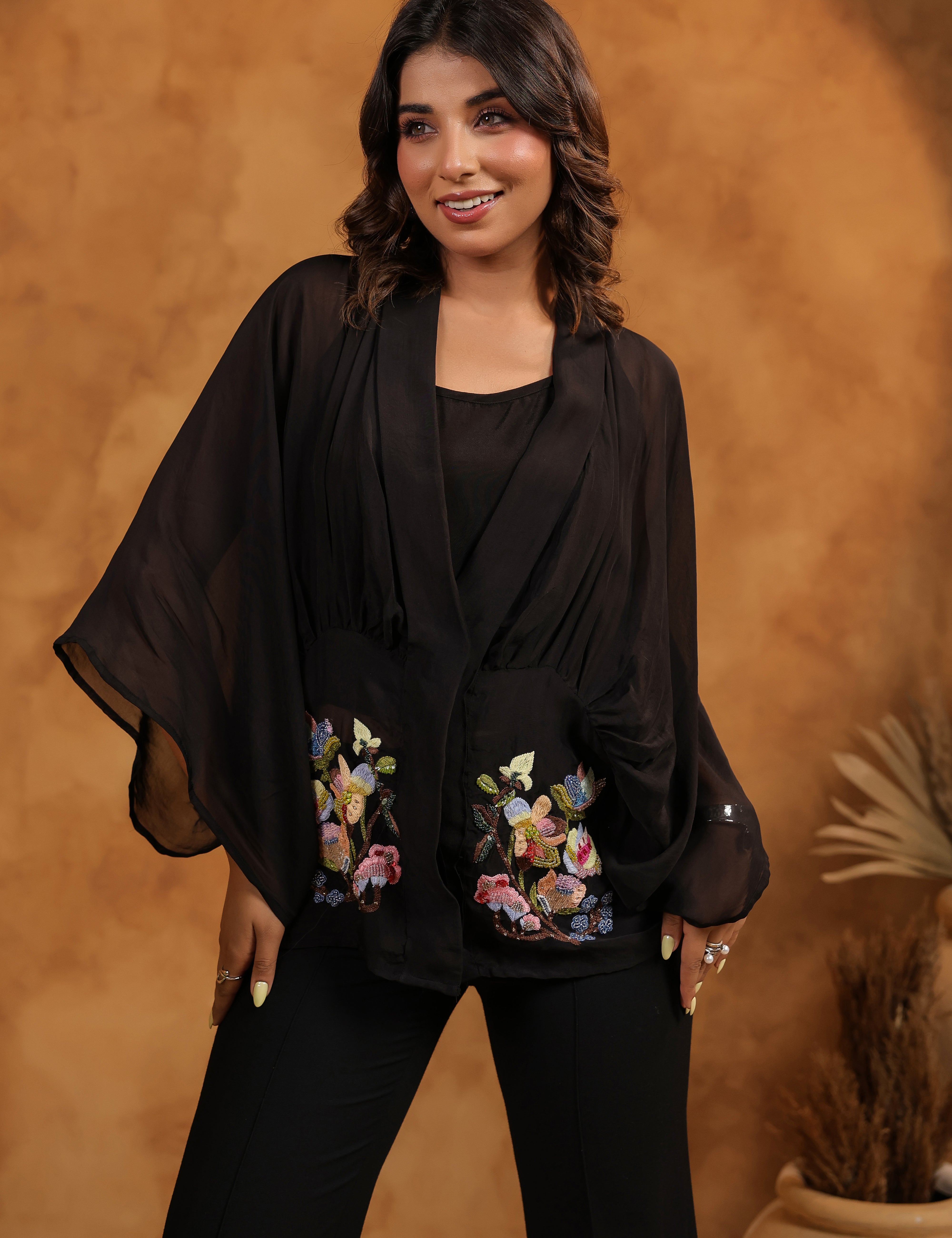 Woman wearing a black outfit with floral embroidery against a warm brown background