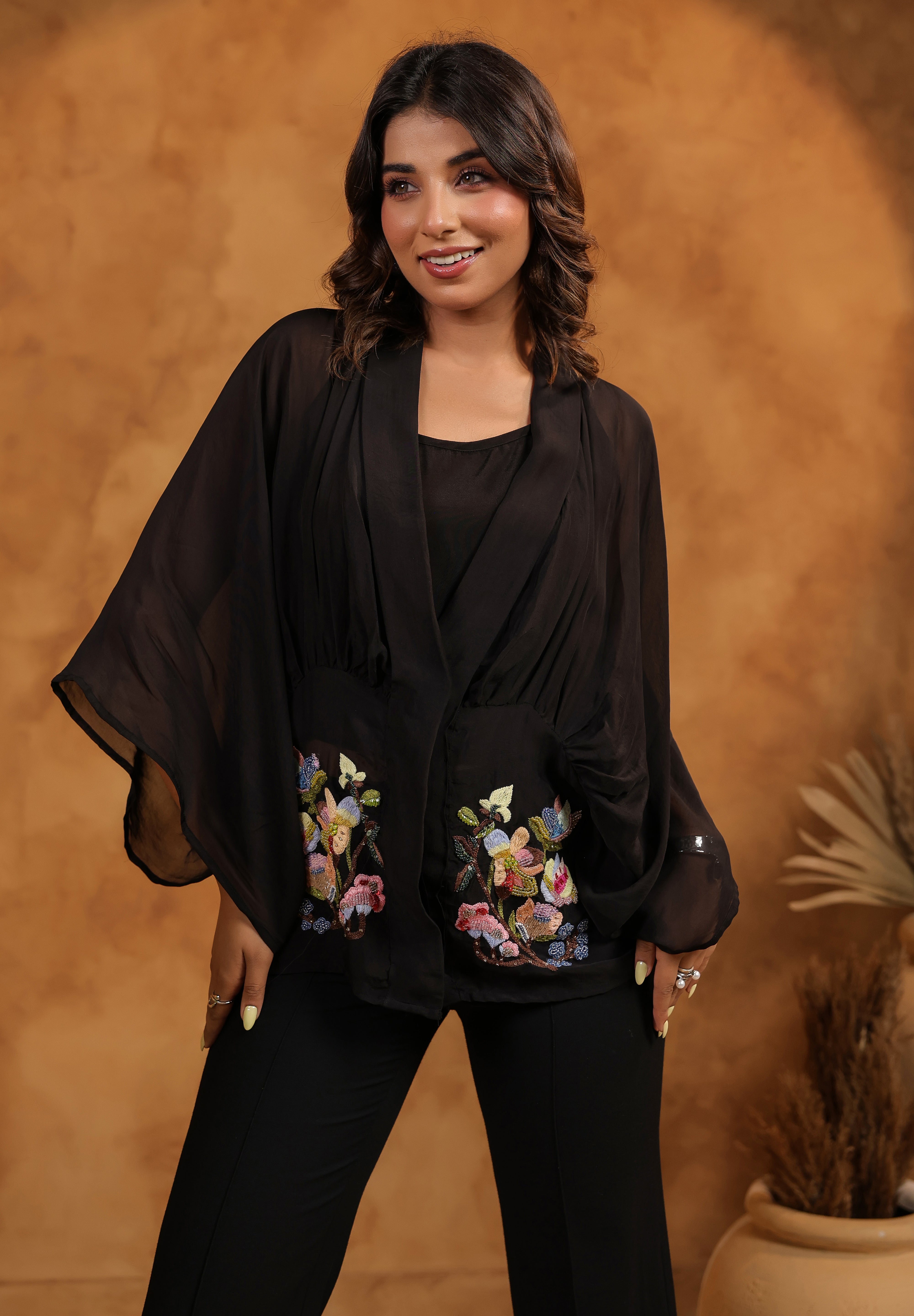 Woman wearing a black outfit with floral embroidery against a warm brown background