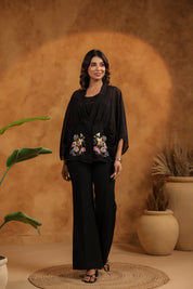 Woman in black outfit with floral embroidery standing against a warm-toned wall with plants.