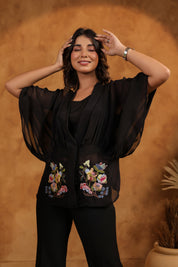 Woman wearing a black outfit with floral embroidery against a brown background