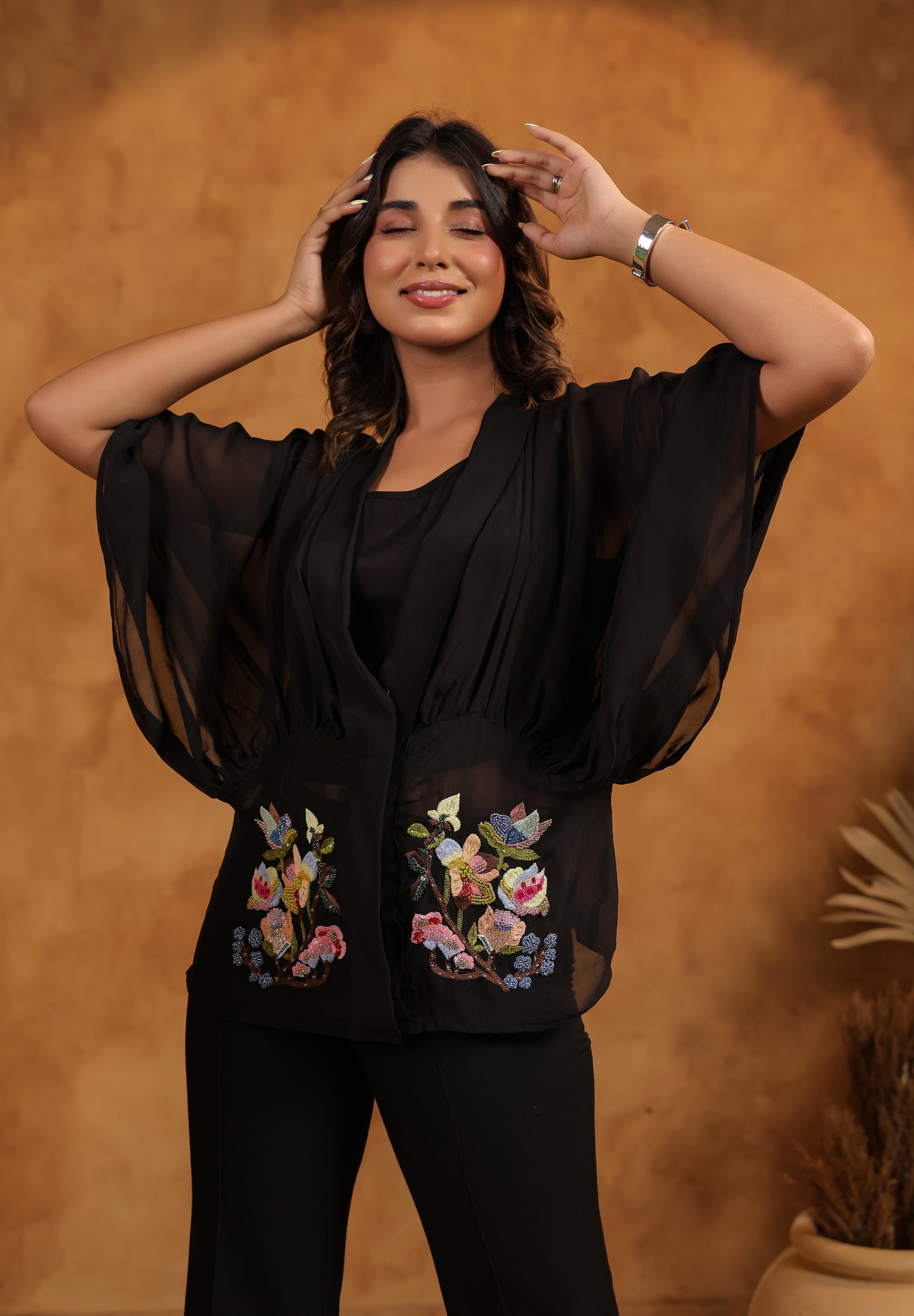 Woman wearing a black outfit with floral embroidery against a brown background