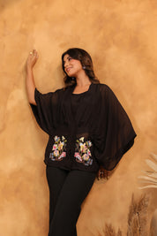 Woman wearing a black top with floral embroidery against a beige wall