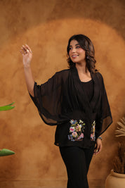 Woman wearing a black outfit with floral embroidery against a brown background