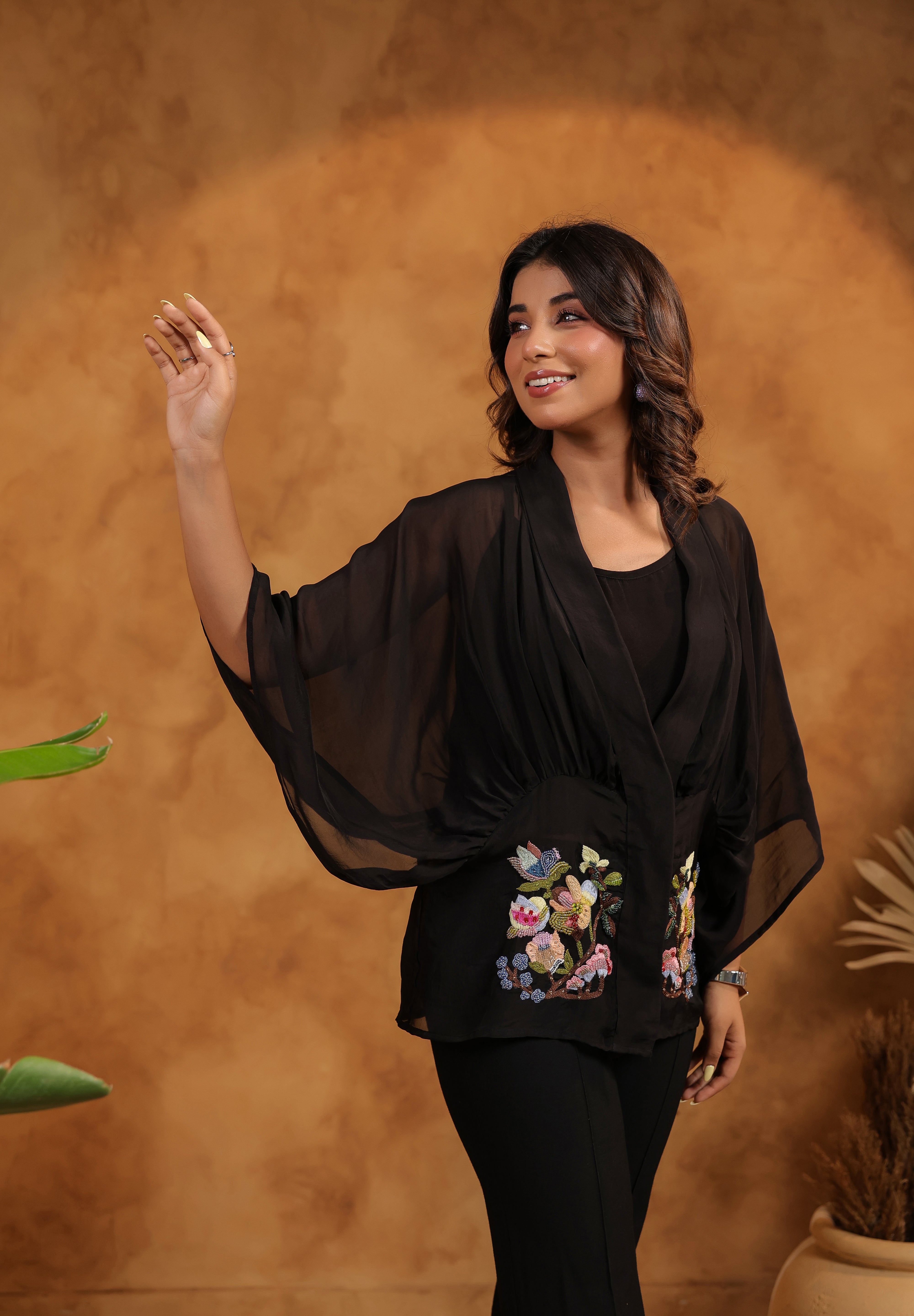 Woman wearing a black outfit with floral embroidery against a brown background