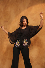 Woman wearing a black outfit with floral embroidery against a brown background