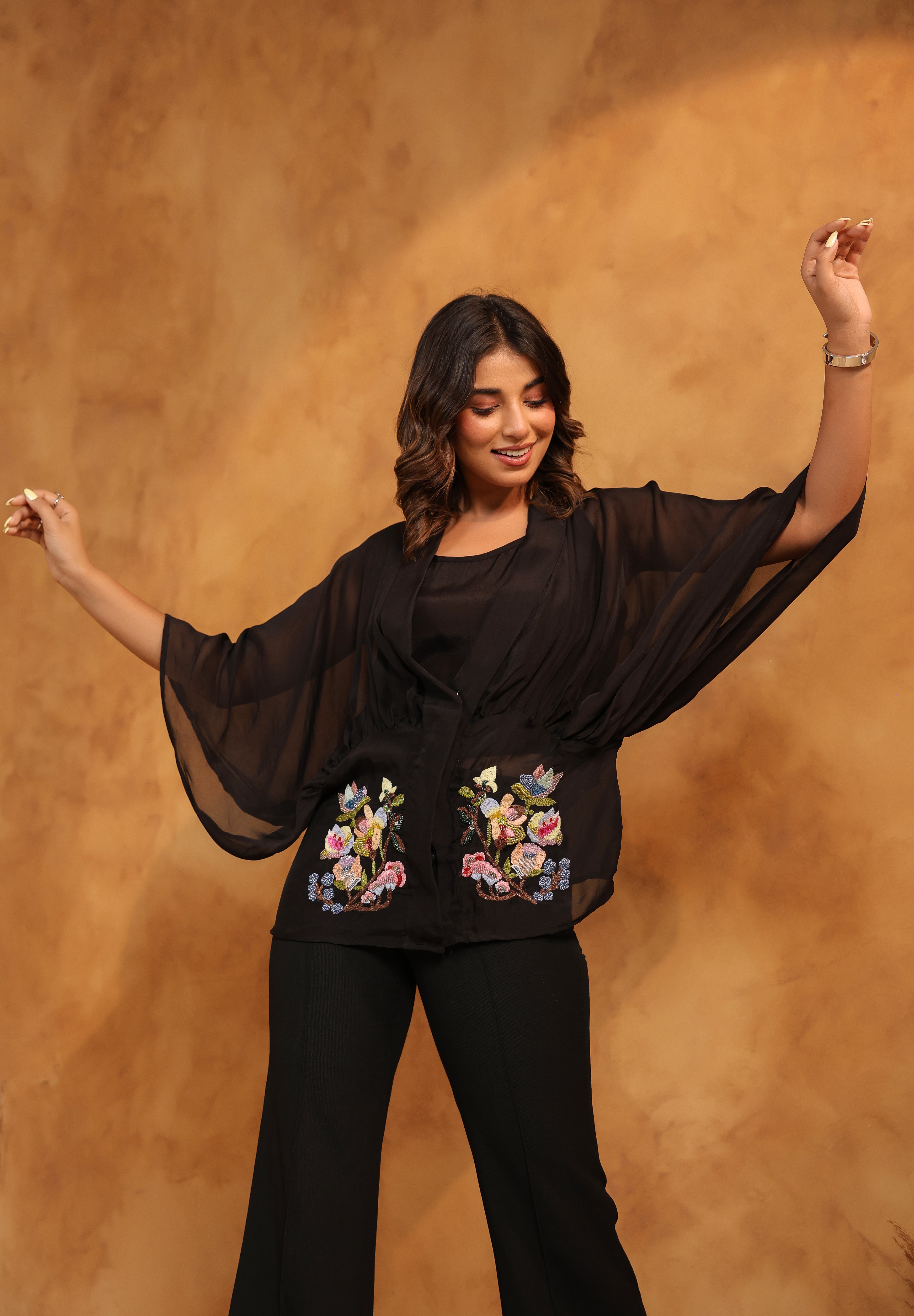 Woman wearing a black outfit with floral embroidery against a brown background