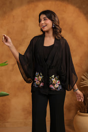 Woman wearing a black outfit with floral embroidery against a warm-toned background