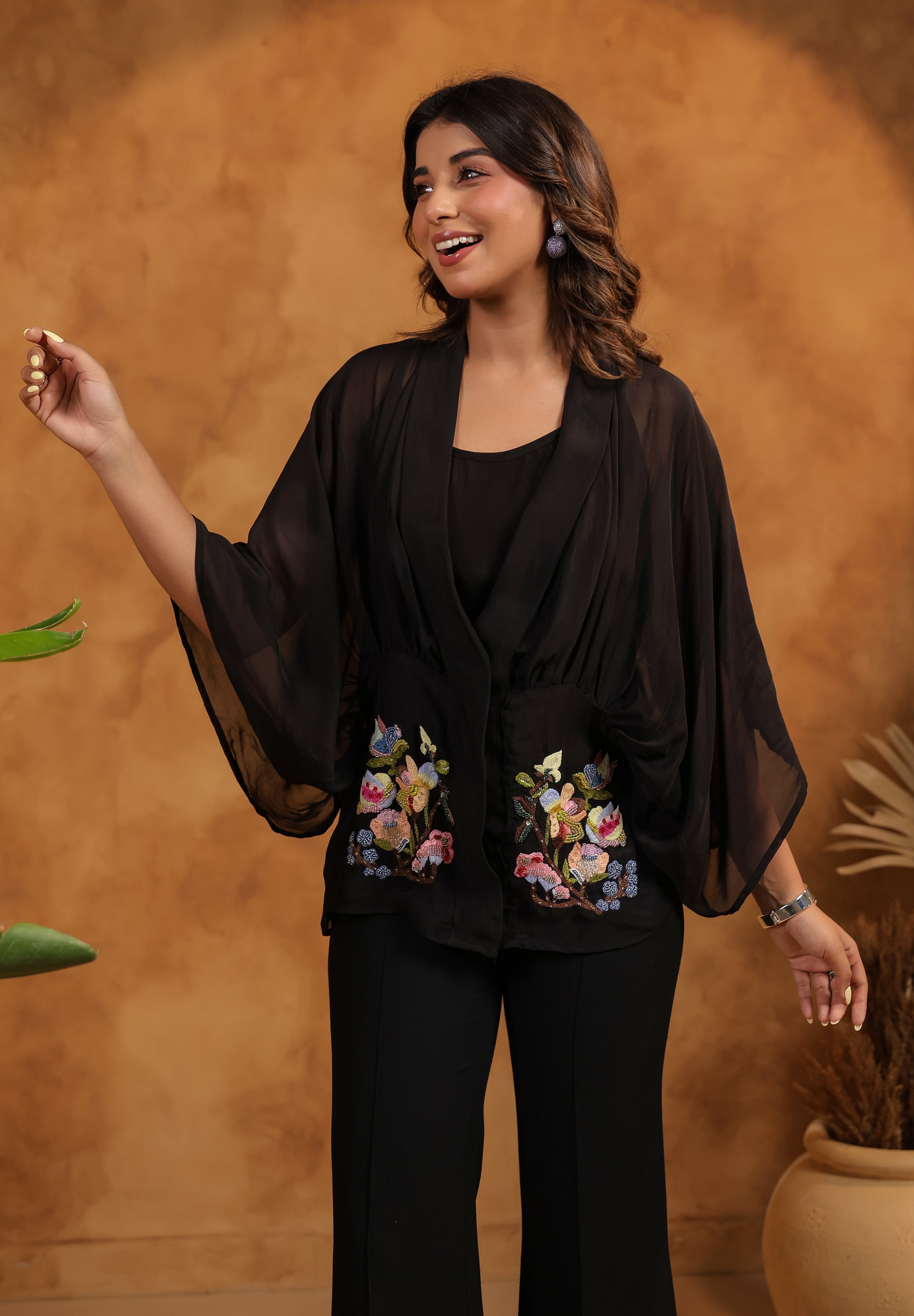 Woman wearing a black outfit with floral embroidery against a warm-toned background