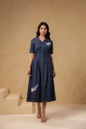 Model wearing Aqua Prism Midi Dress, denim A-line silhouette with turtle embroidery on bodice and skirt, front view