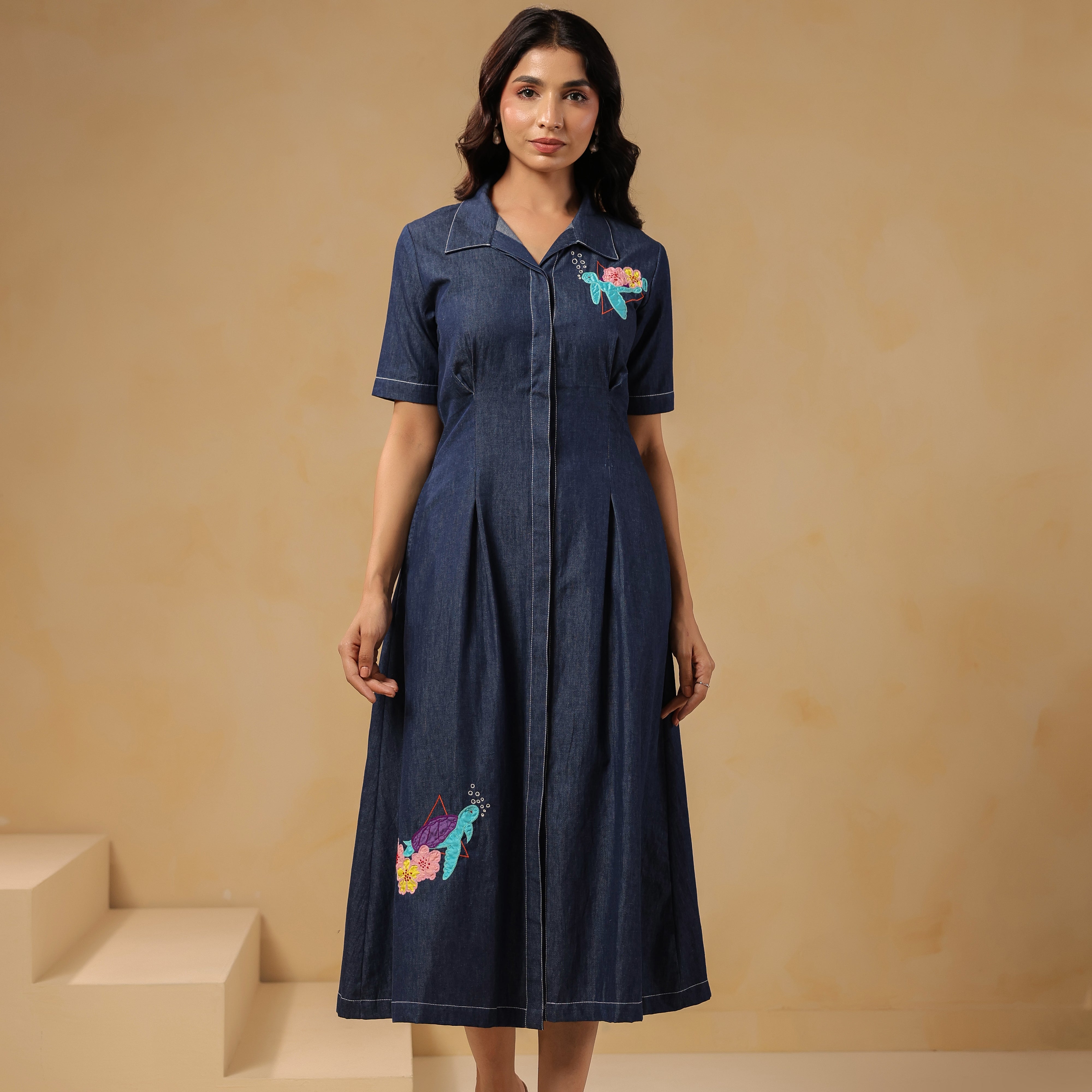 Model wearing Aqua Prism Midi Dress, denim A-line silhouette with turtle embroidery on bodice and skirt, front view