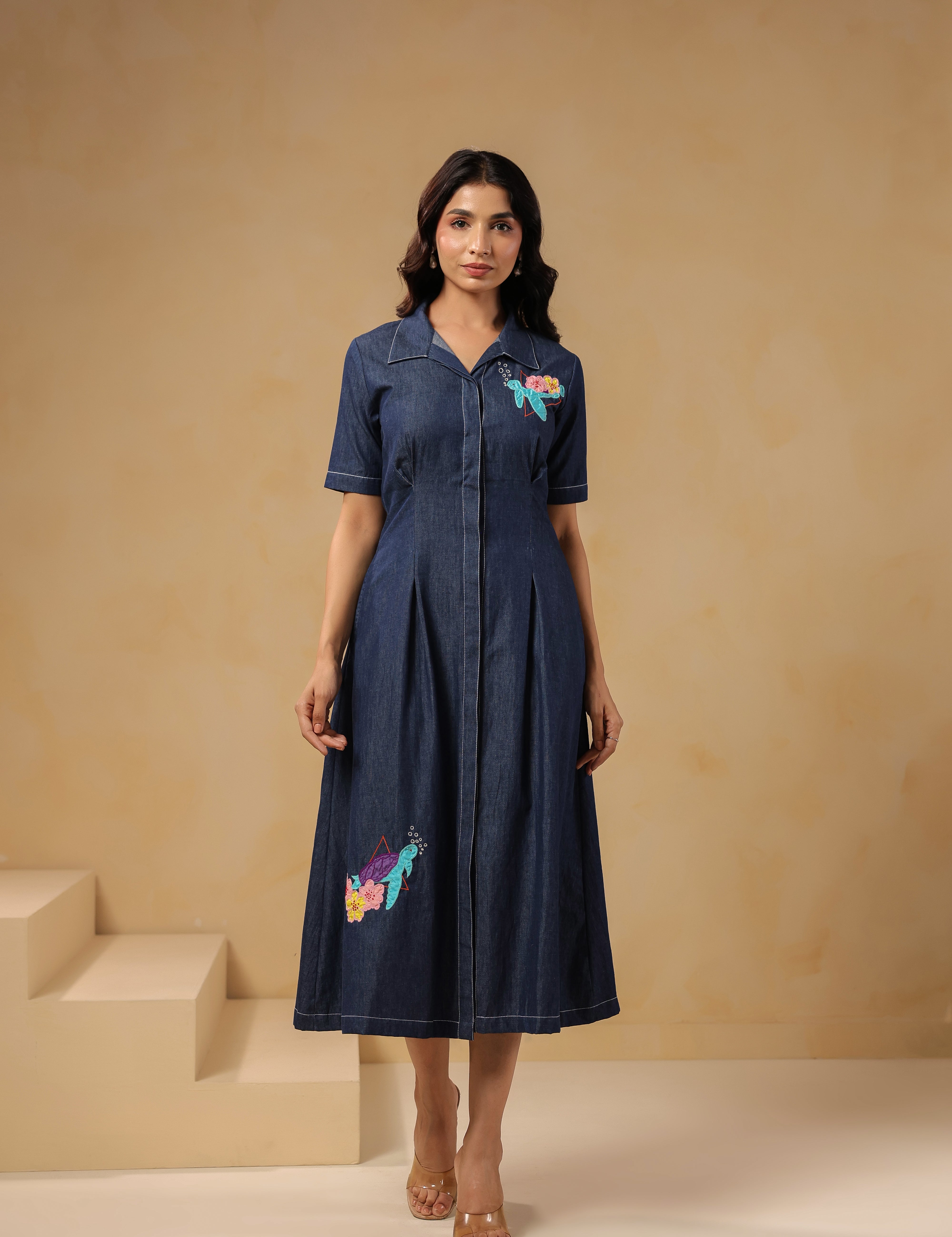 Model wearing Aqua Prism Midi Dress, denim A-line silhouette with turtle embroidery on bodice and skirt, front view