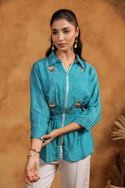 Woman wearing a blue shirt with embroidery  against a brown background