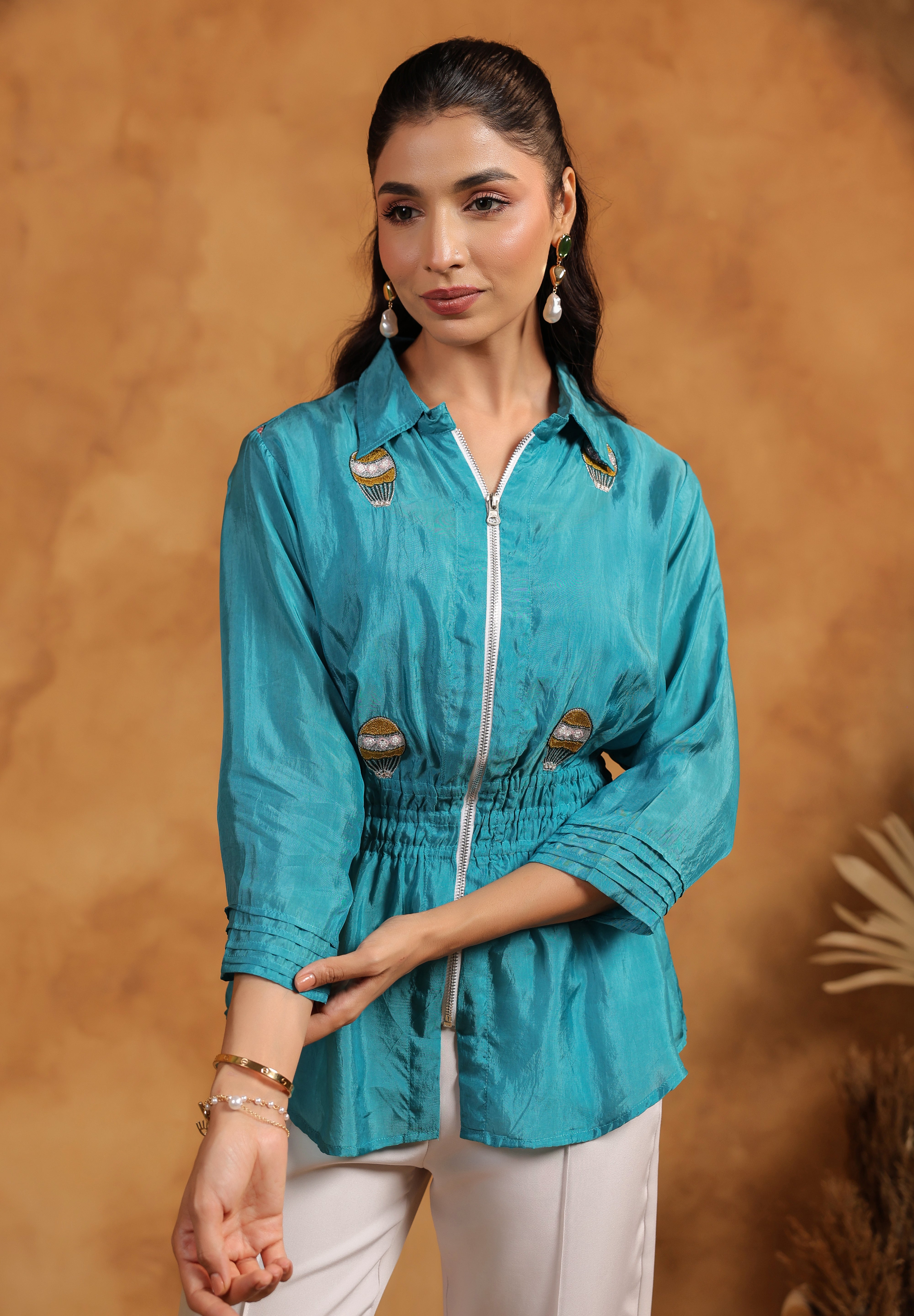 Woman wearing a blue shirt with embroidery  against a brown background