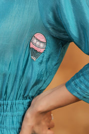 Teal fabric with a pink and black embroidered design of a hot air balloon.