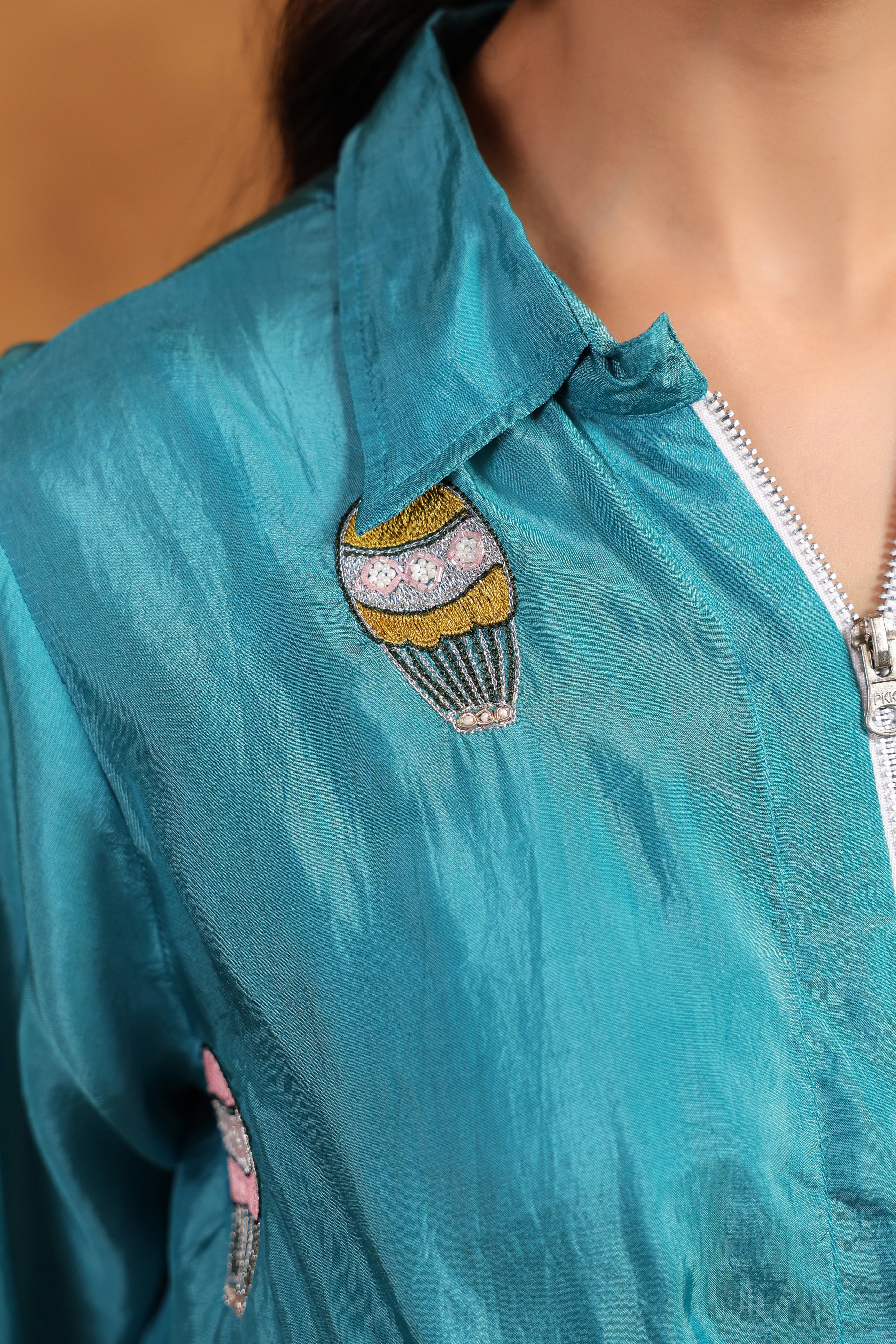 Teal shirt with a decorative brooch featuring a colorful design.