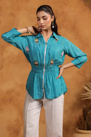 Woman wearing a turquoise top with white pants against a brown background