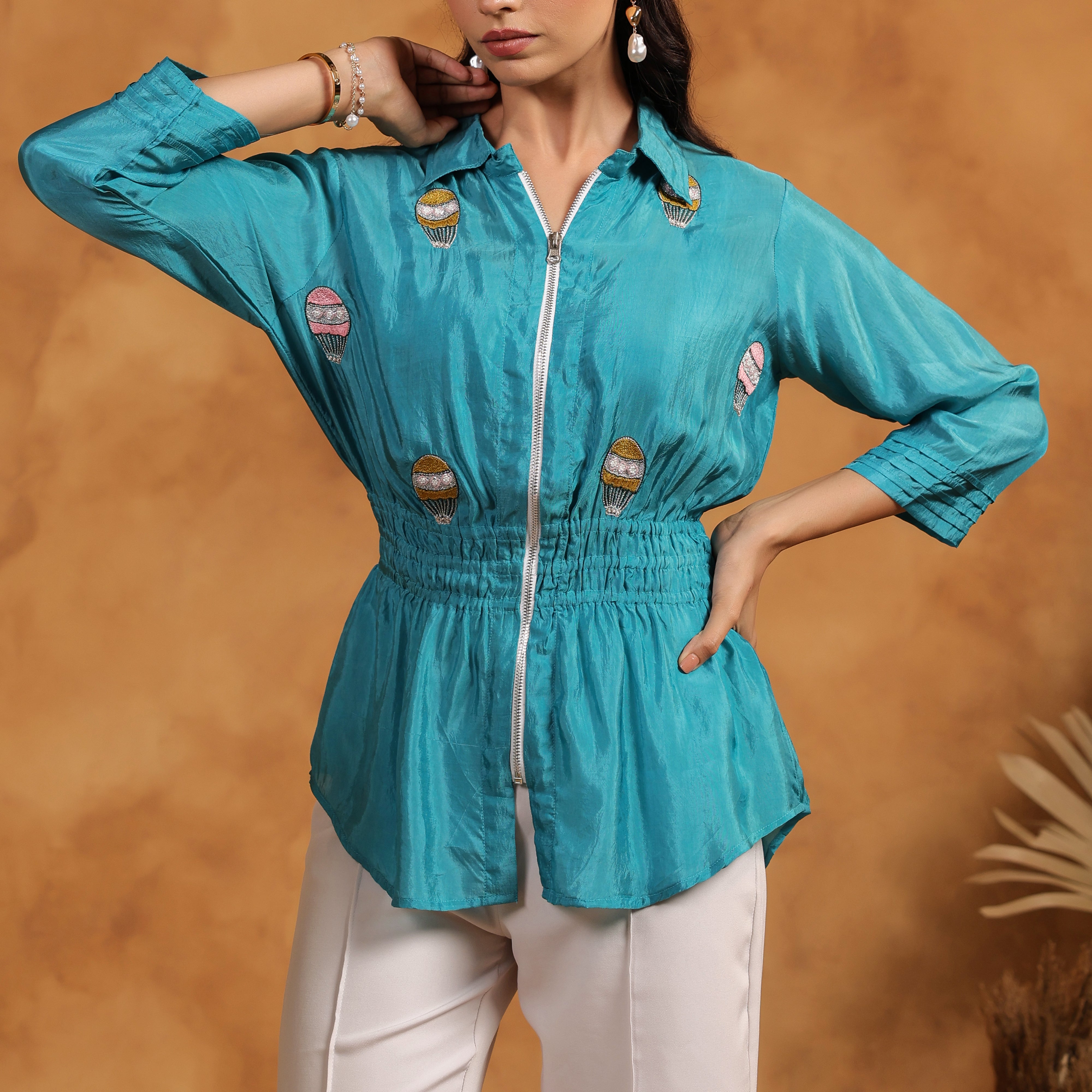 Woman wearing a turquoise top with white pants against a brown background