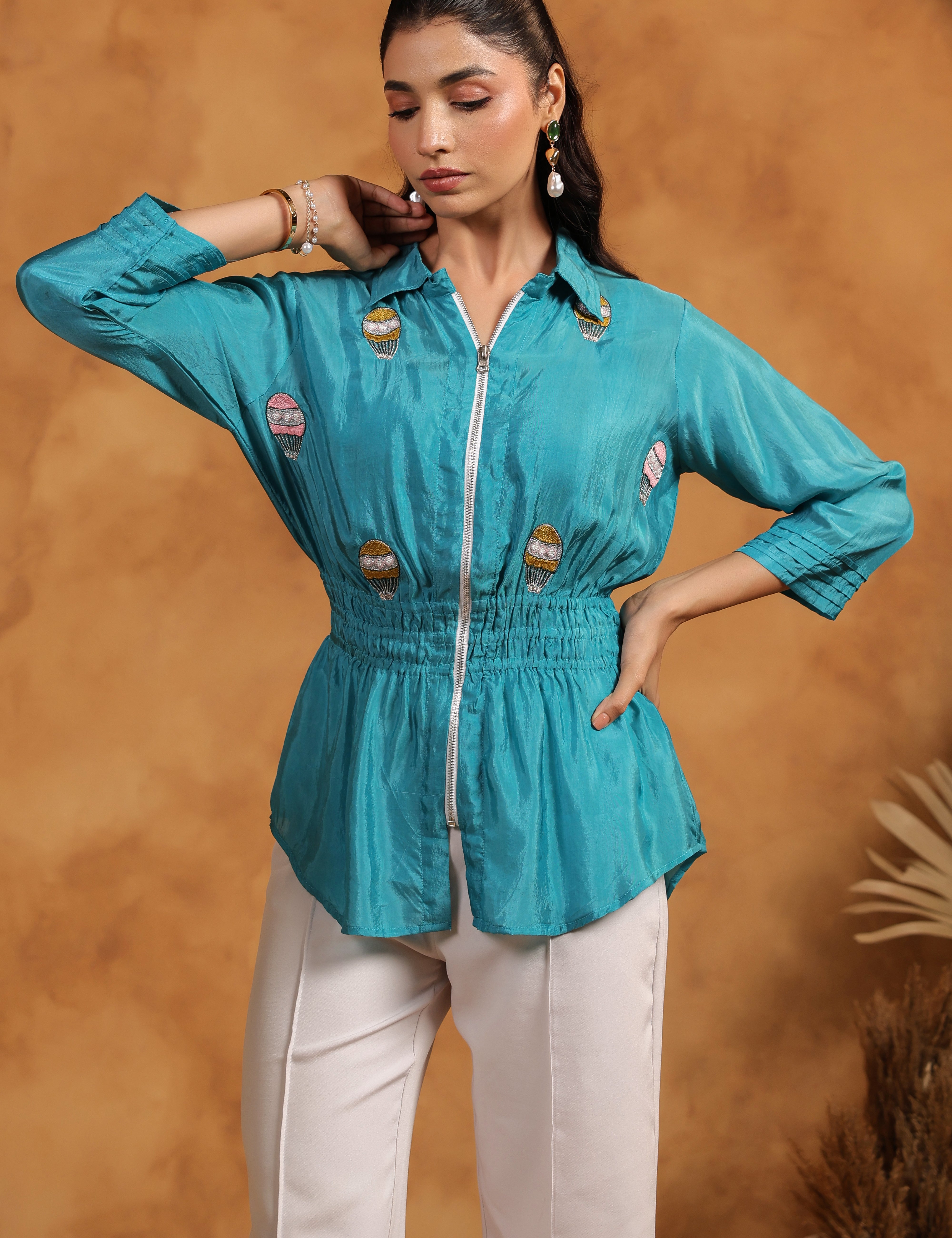 Woman wearing a turquoise top with white pants against a brown background