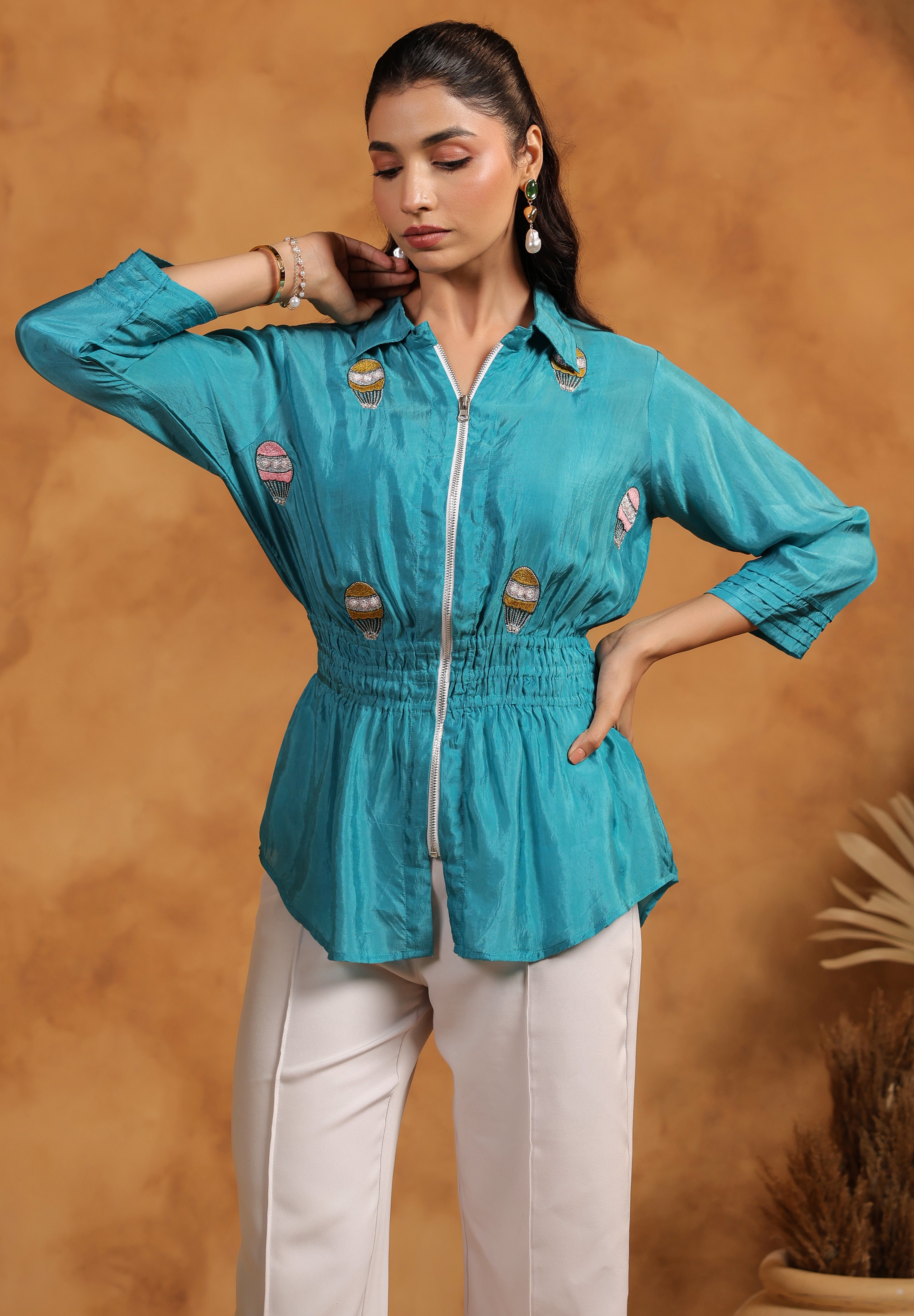Woman wearing a turquoise top with white pants against a brown background