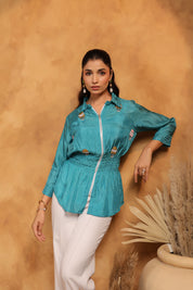 Woman wearing a teal jacket with white pants against a beige background