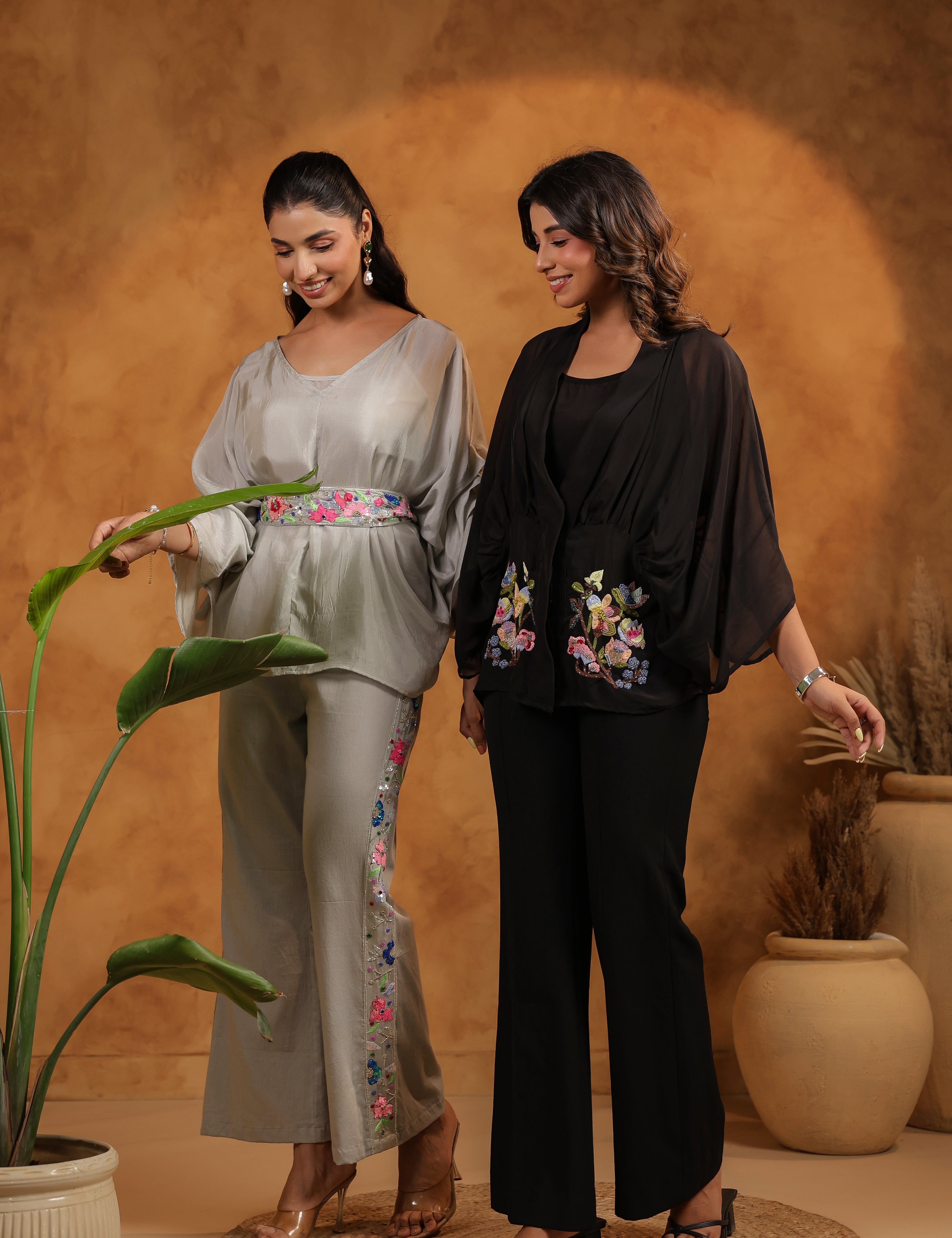 Two women in stylish outfits standing in a room with a textured wall and potted plants.
