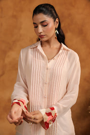 Woman wearing a light-colored shirt with decorative cuffs against a warm brown background