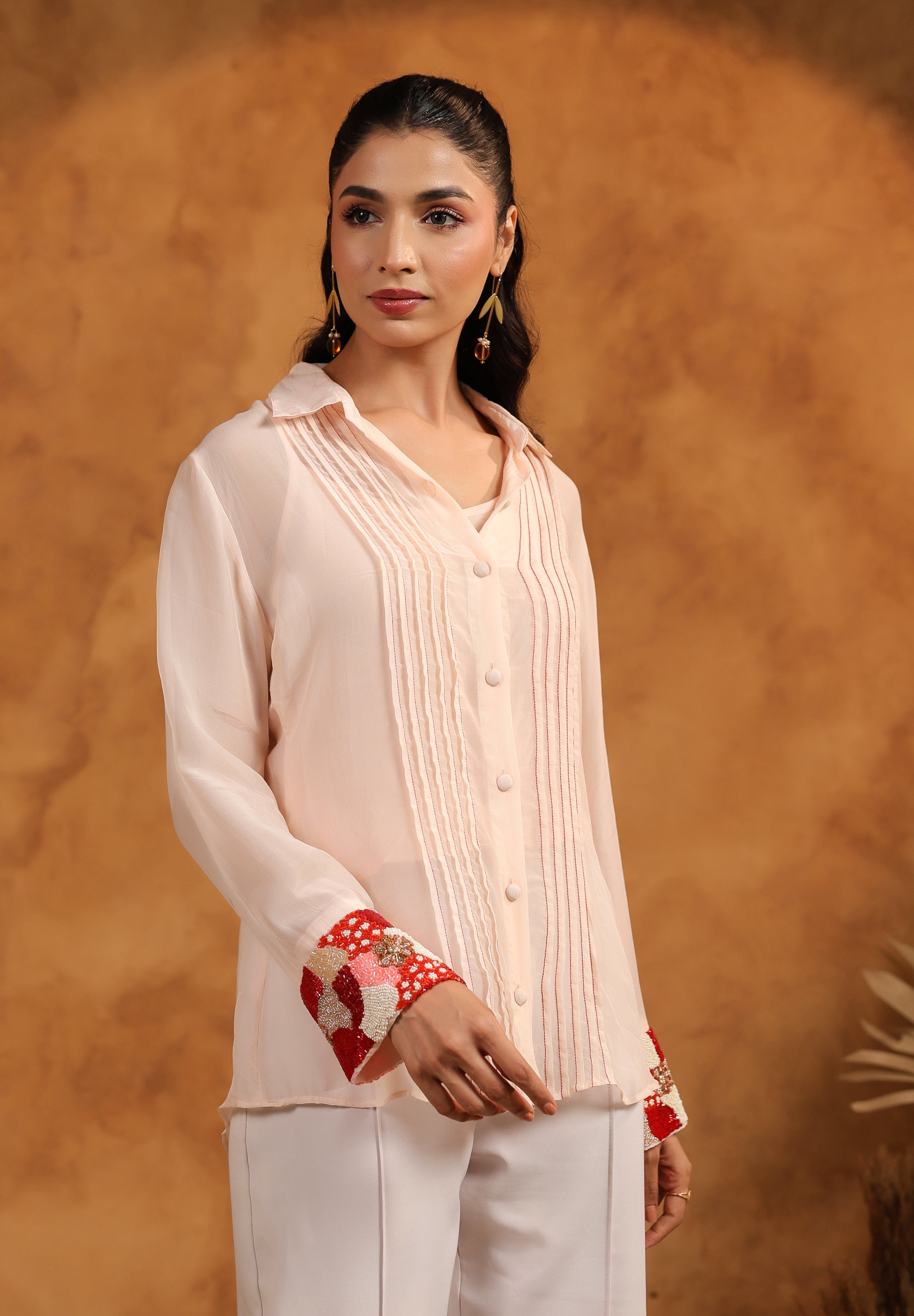 Woman wearing a light-colored outfit with red accents against a brown background