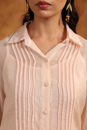 Close-up of a person wearing a light pink pin tuck shirt with a blurred background