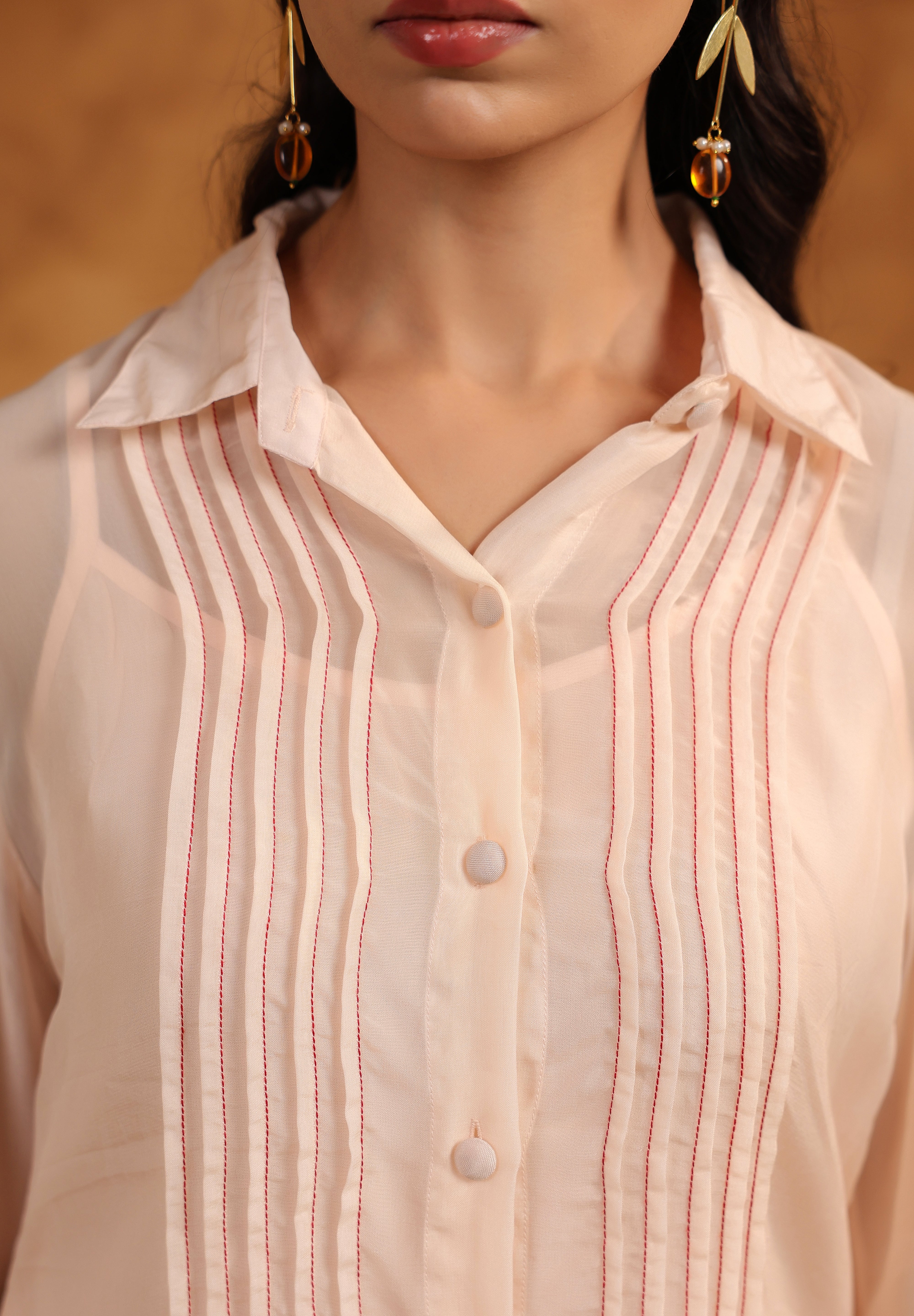 Close-up of a person wearing a light pink pin tuck shirt with a blurred background