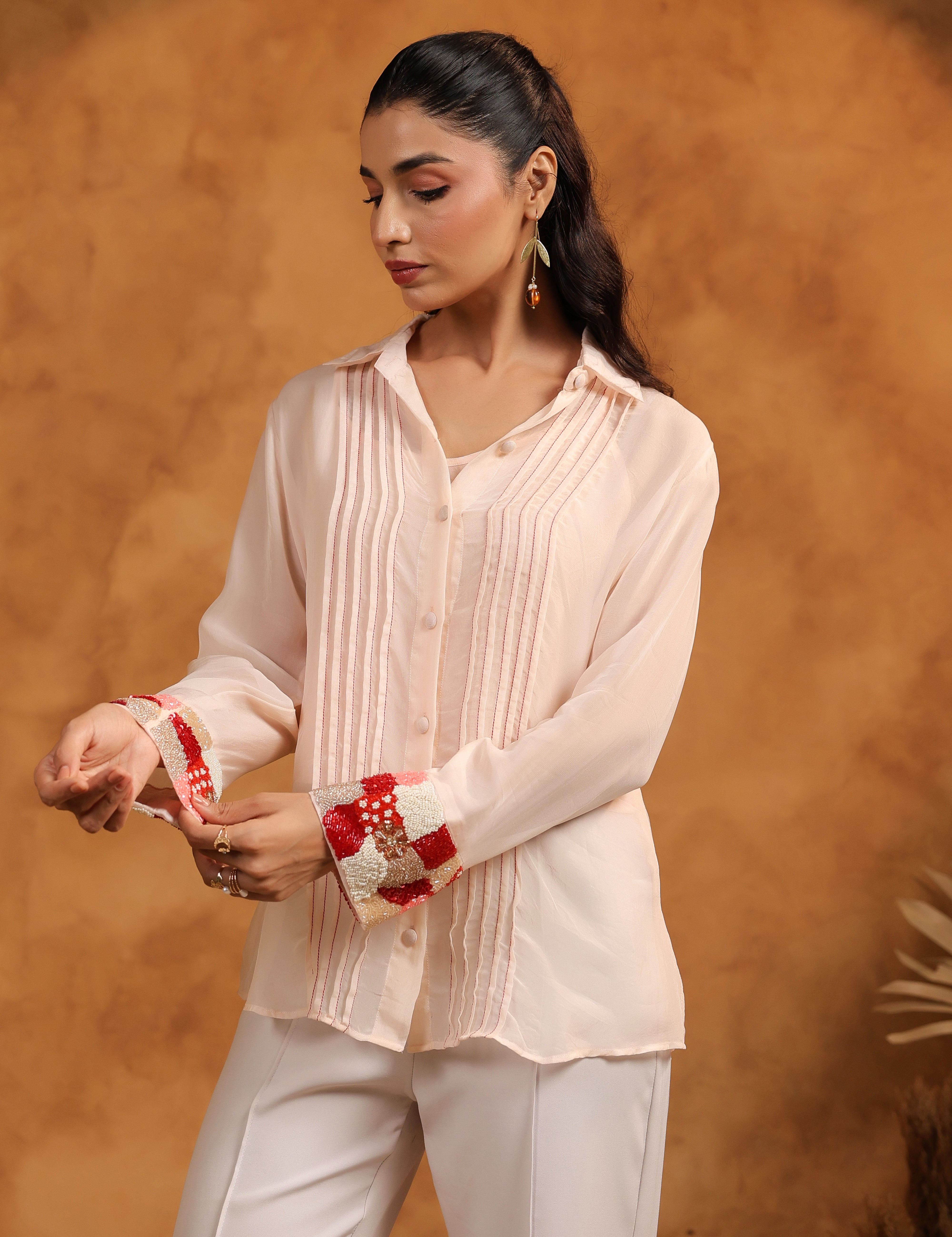 Woman wearing a light pink blouse and white pants against a warm brown background