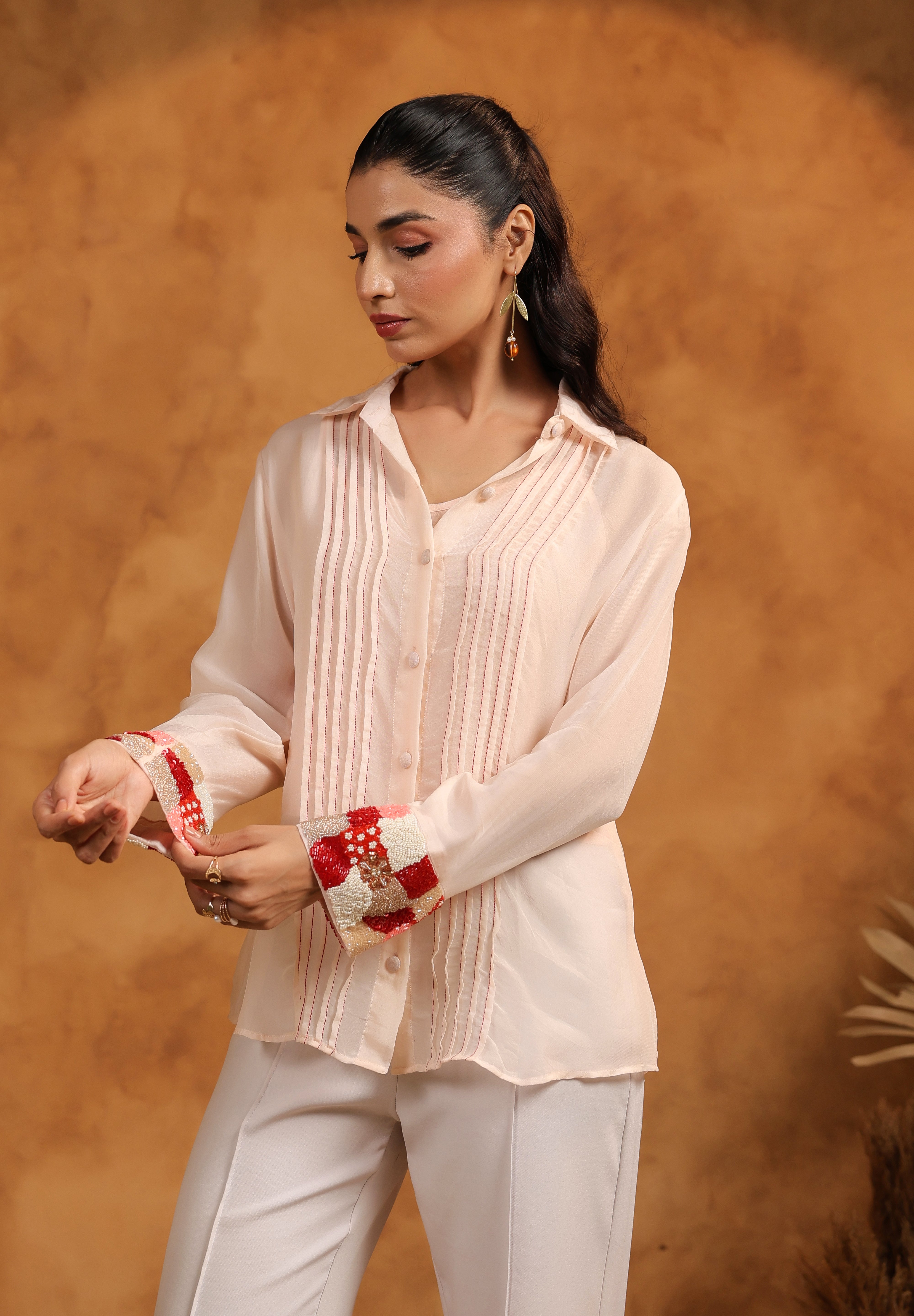 Woman wearing a light pink blouse and white pants against a warm brown background