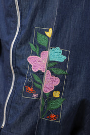 Detailed view of the geometric floral embroidery with vibrant pink, yellow, and blue blooms on denim