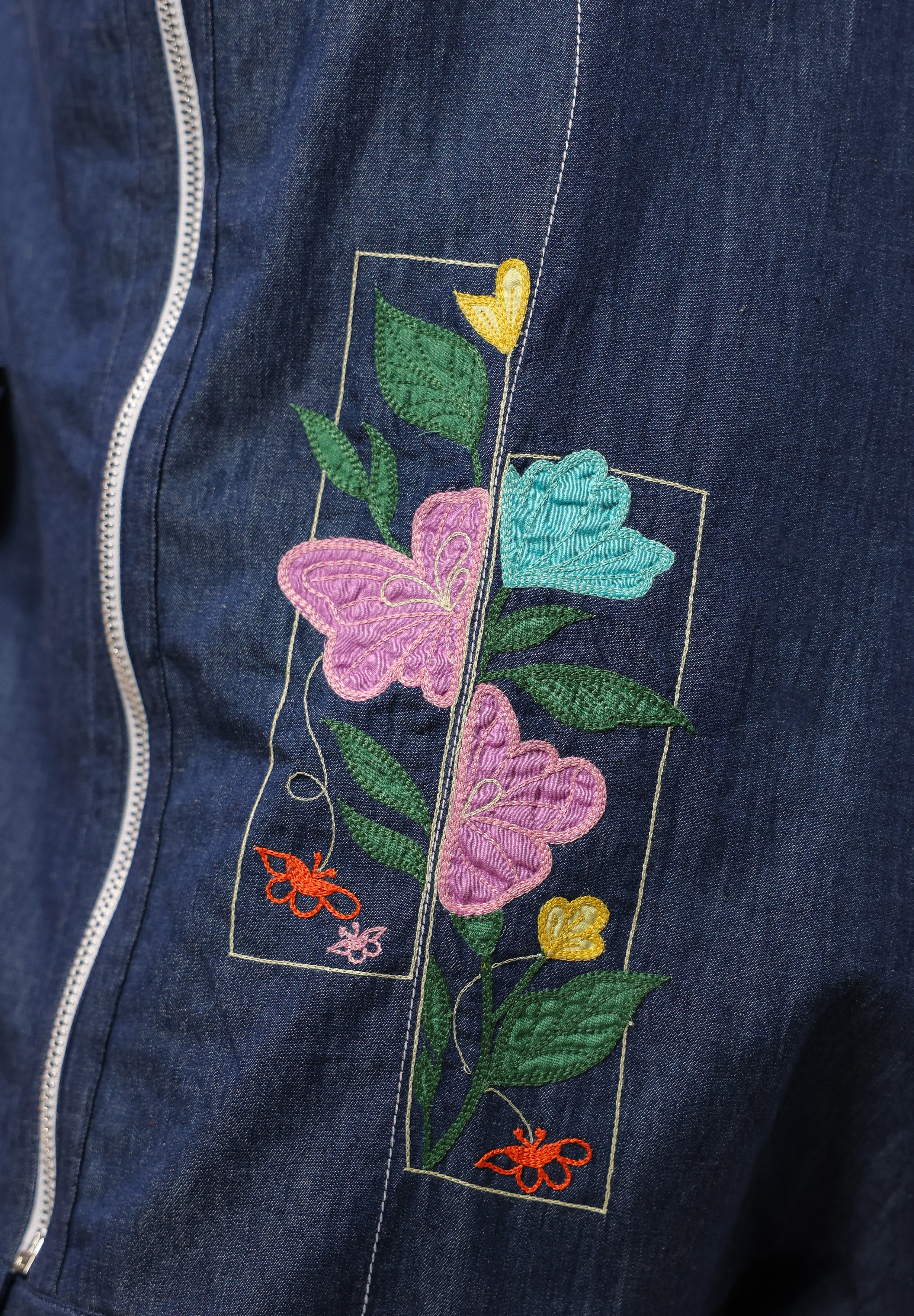 Detailed view of the geometric floral embroidery with vibrant pink, yellow, and blue blooms on denim