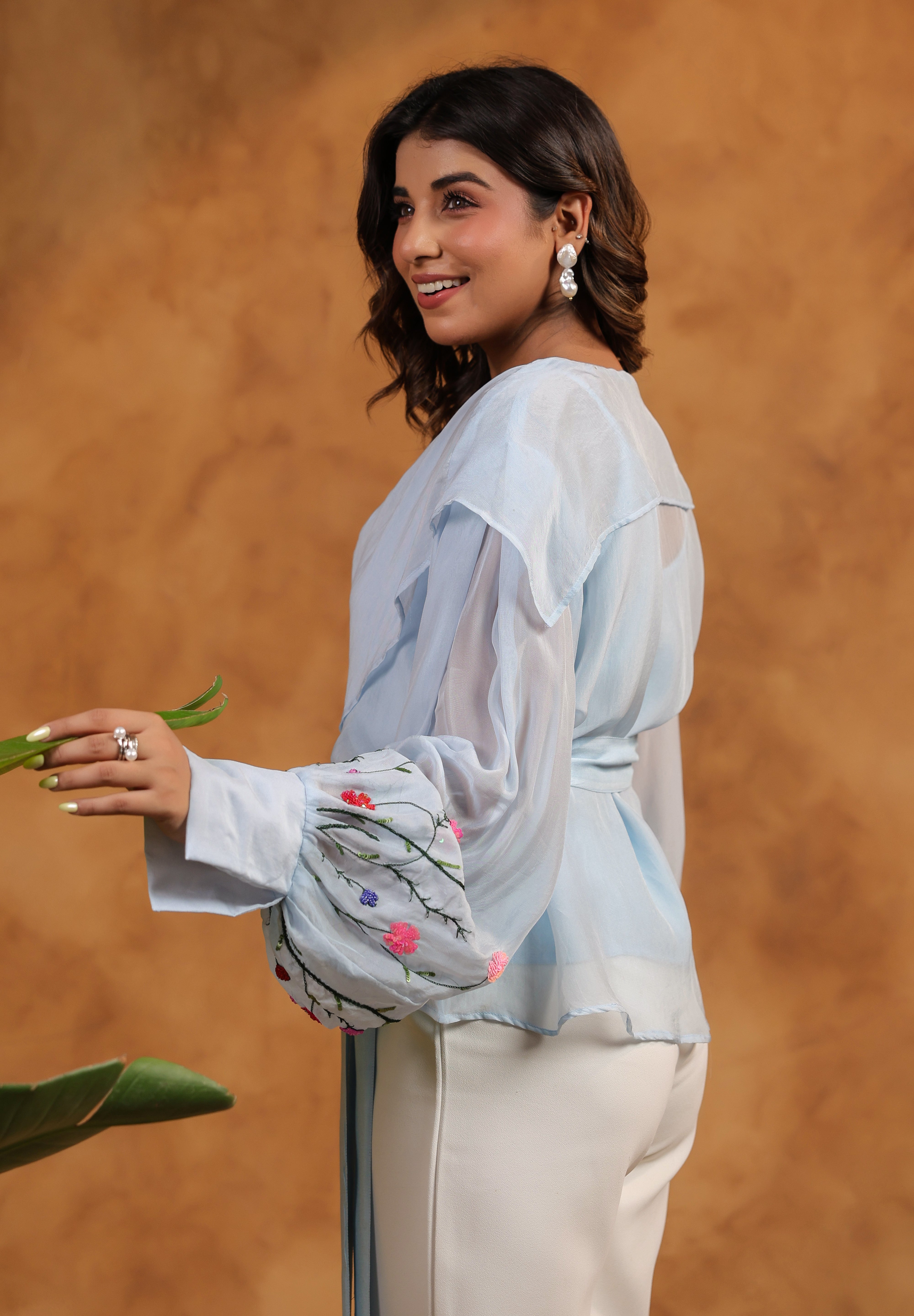 Woman wearing a light blue blouse with sheer sleeves against an orange background