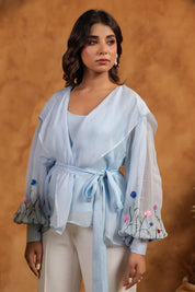 Woman wearing a light blue embroidered top against a brown background