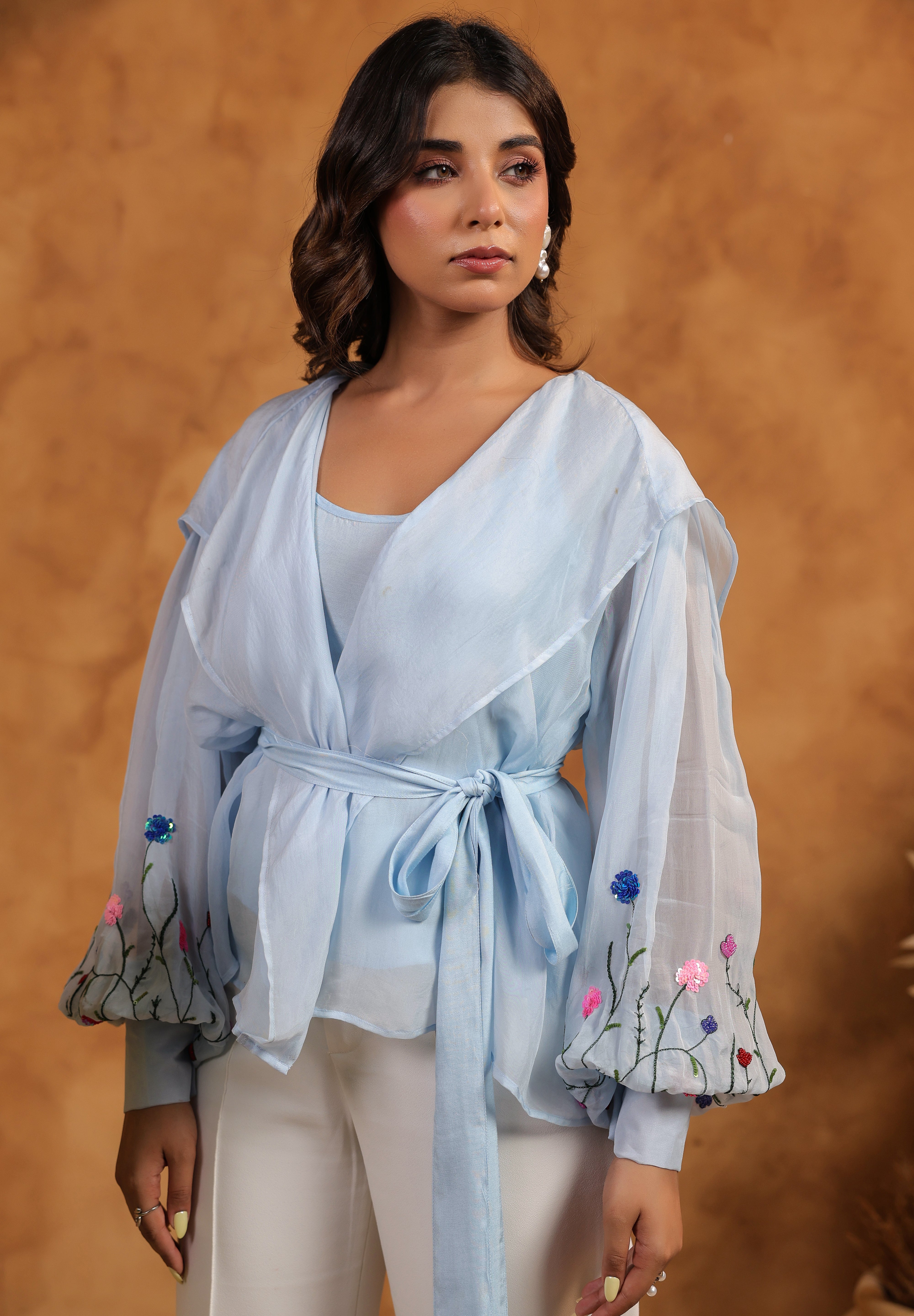 Woman wearing a light blue embroidered top against a brown background