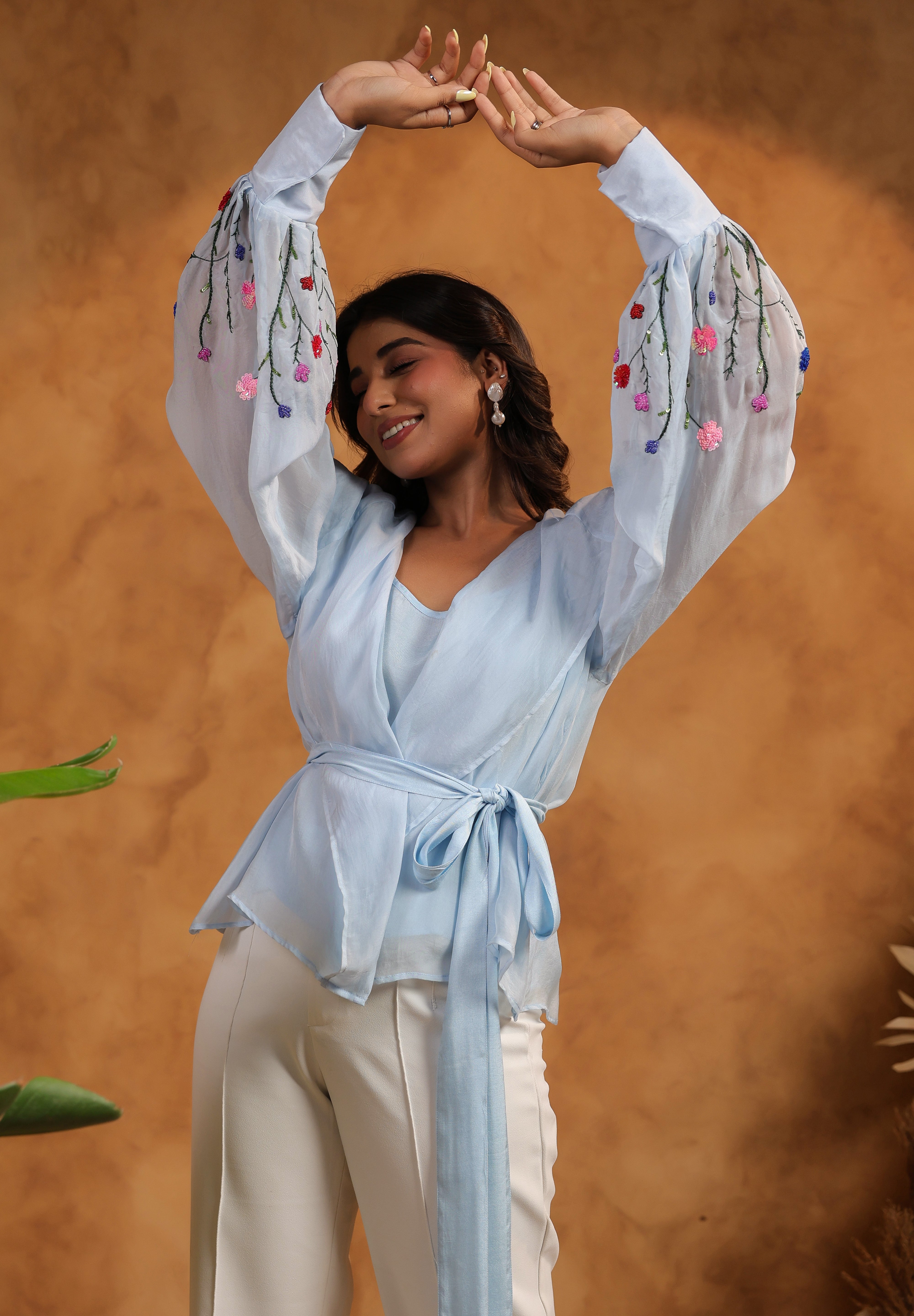 Woman wearing a light blue outfit with floral embellishments against an orange background