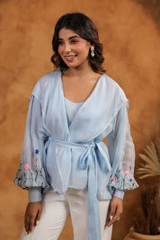 Woman wearing a light blue top with floral embroidery against a brown background