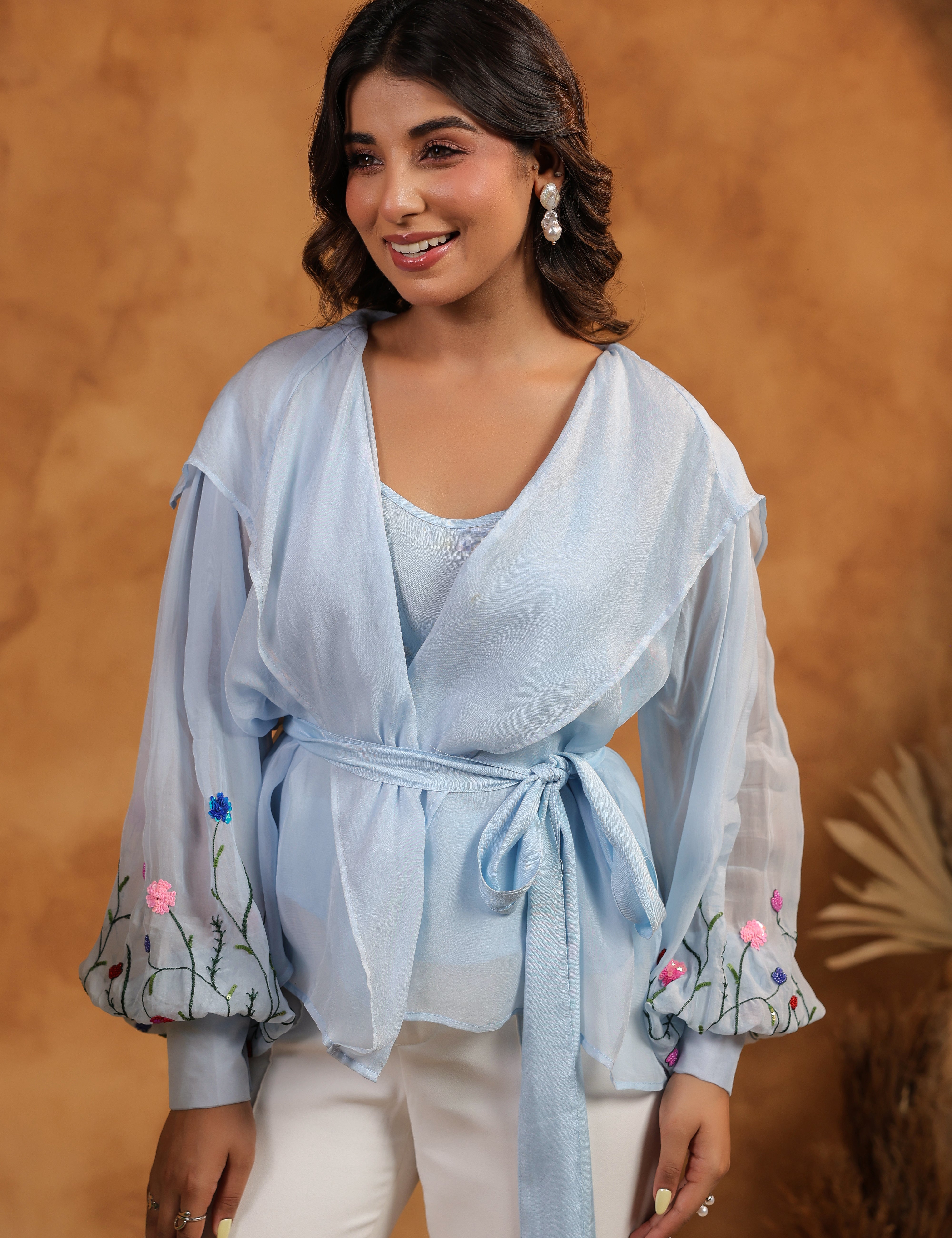 Woman wearing a light blue top with floral embroidery against a brown background