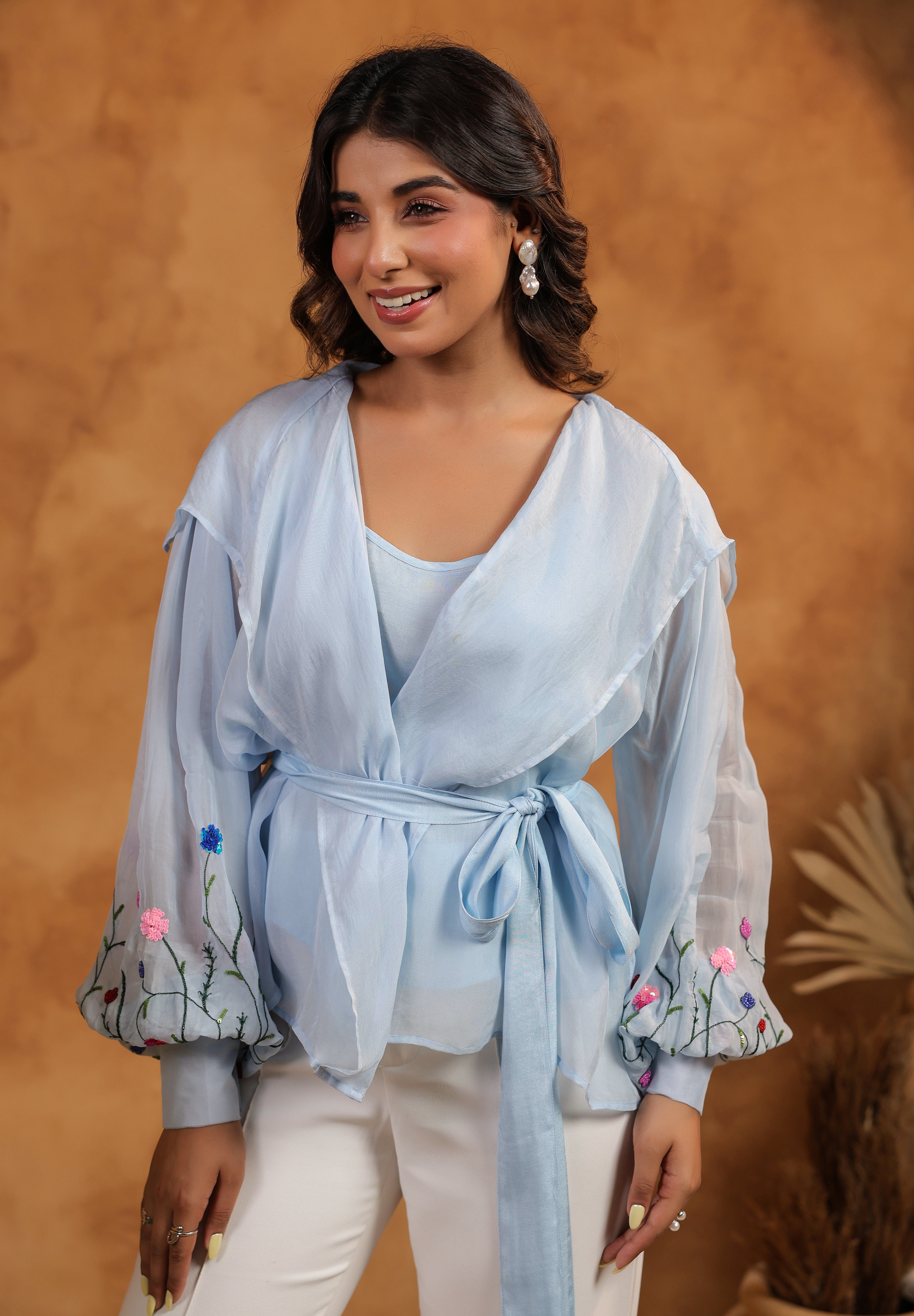 Woman wearing a light blue top with floral embroidery against a brown background