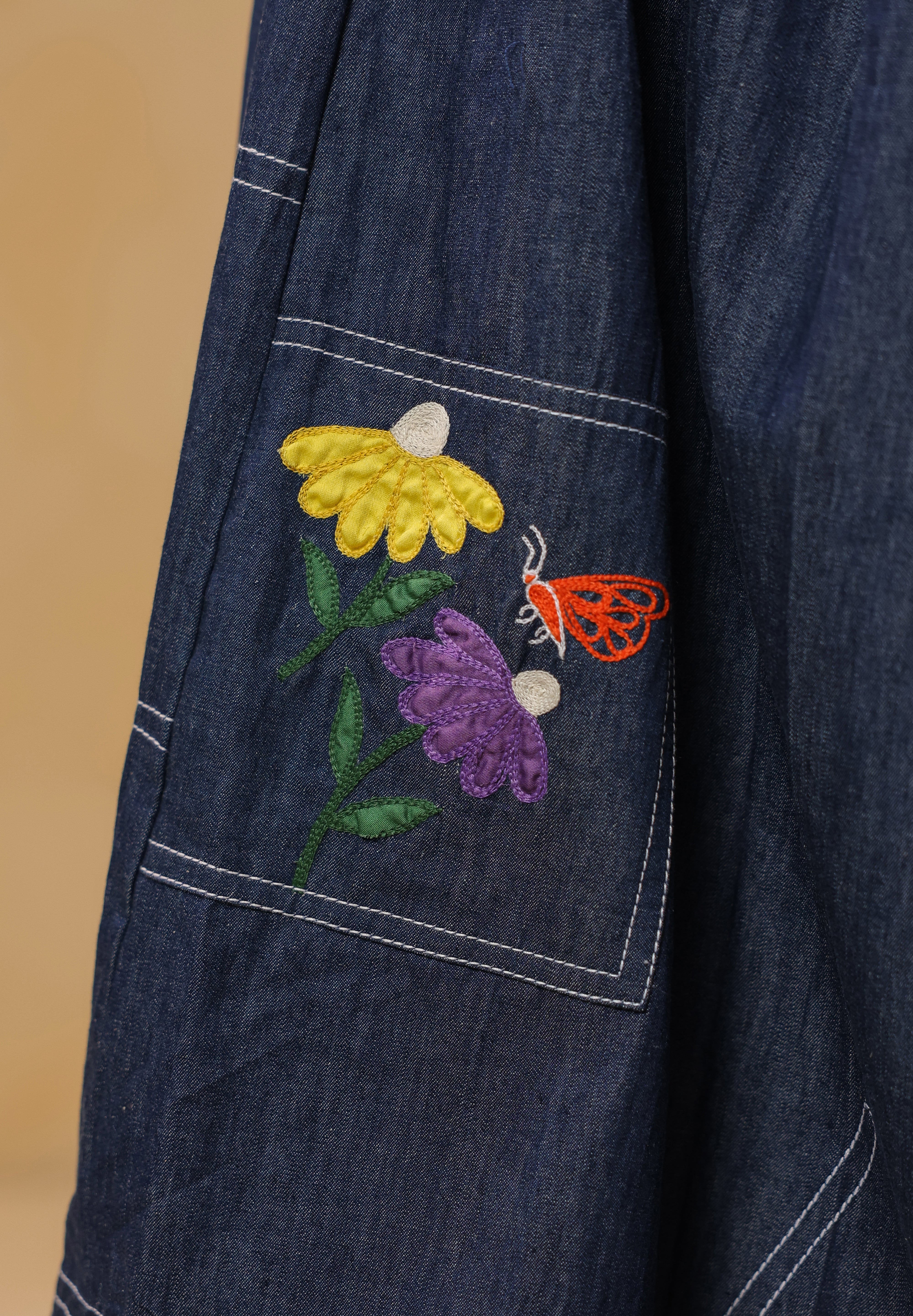 Close-up of pocket patch embroidery featuring yellow and purple florals with an orange butterfly — inspired by meadows in bloom.